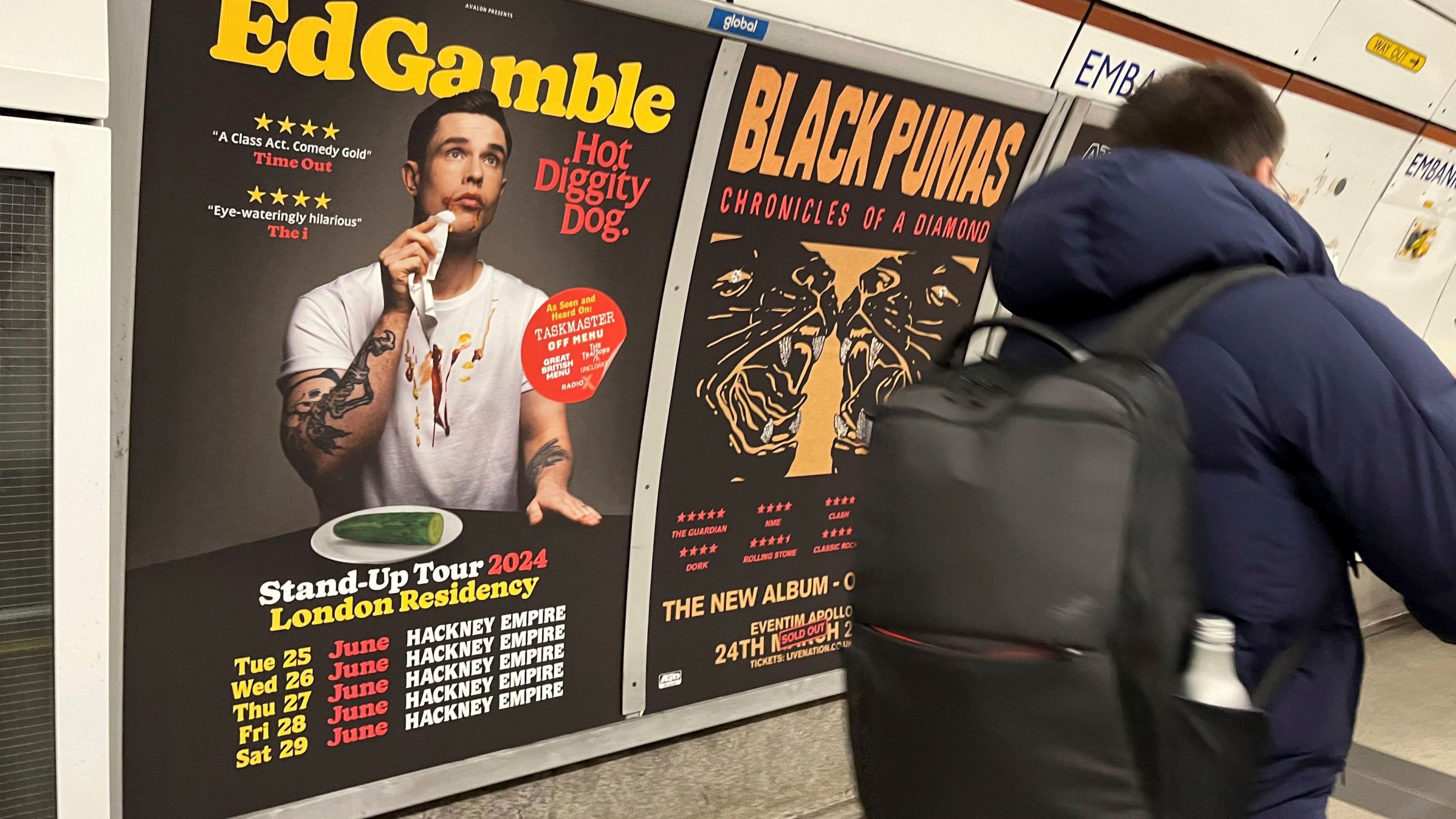 A view of a poster advertising comedian Ed Gamble's Hot Diggity Dog tour on the Bakerloo line platform at Embankment underground station in London, Wednesday March 27, 2024. Gamble has been ordered to change a subway station poster campaign for his new standup show because the image of a hot dog violated the transit network’s ban on junk food advertising. The poster for the show, “Hot Diggity Dog,” showed a mustard- and ketchup-smeared Gamble beside a half-eaten hot dog on a plate. A bemused Gamble replaced the wiener with a cucumber, and the poster was approved. (Joe Sene/PA via AP)