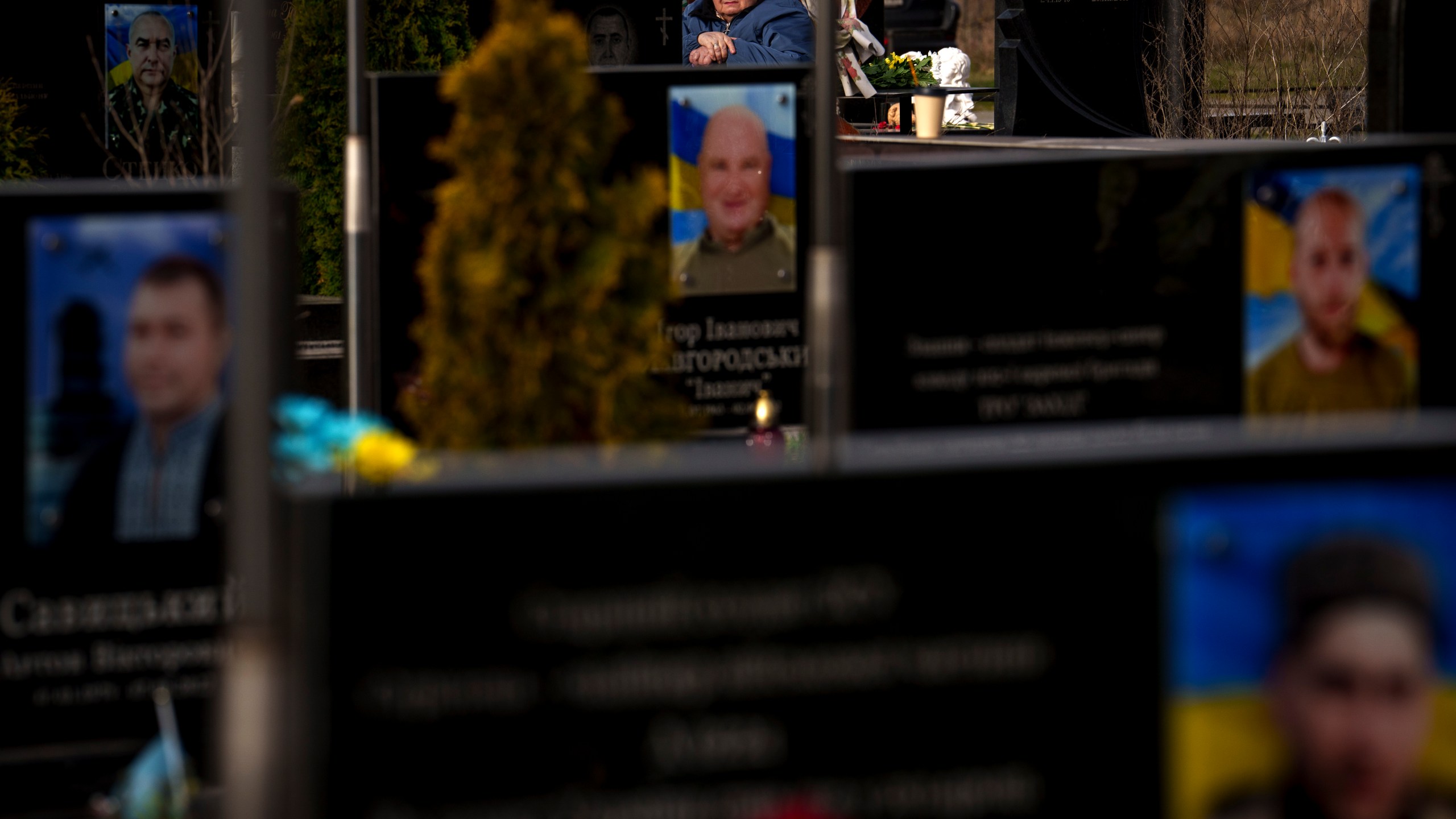 A woman sits behind graves of Ukrainian servicemen and civilians killed during the Russian occupation during a commemoration of the victims at a cemetery in Bucha, Ukraine, Sunday, March 31, 2024. Ukrainians mark the second anniversary of the liberation of Bucha, during which Russian occupation left hundreds of civilians dead in the streets and in mass graves in Bucha during the initial months of the Russian invasion in 2022. (AP Photo/Vadim Ghirda)