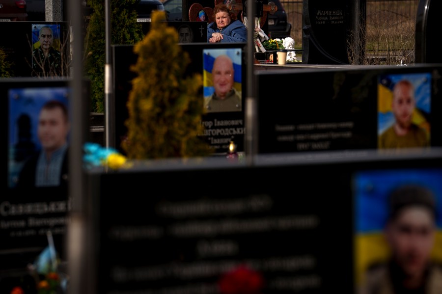 A woman sits behind graves of Ukrainian servicemen and civilians killed during the Russian occupation during a commemoration of the victims at a cemetery in Bucha, Ukraine, Sunday, March 31, 2024. Ukrainians mark the second anniversary of the liberation of Bucha, during which Russian occupation left hundreds of civilians dead in the streets and in mass graves in Bucha during the initial months of the Russian invasion in 2022. (AP Photo/Vadim Ghirda)