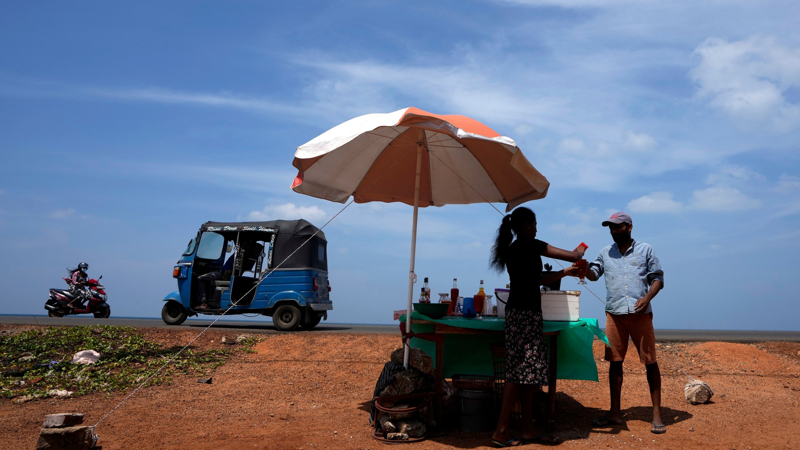 FILE - A man buys a cool drink from a roadside vendor on a sunny day in Mahawewa, a village north of Colombo, Sri Lanka, Feb. 29, 2024. A new study says climate change will reduce future global income by about 19% in the next 25 years compared to a fictional world that’s not warming. (AP Photo/Eranga Jayawardena, File)