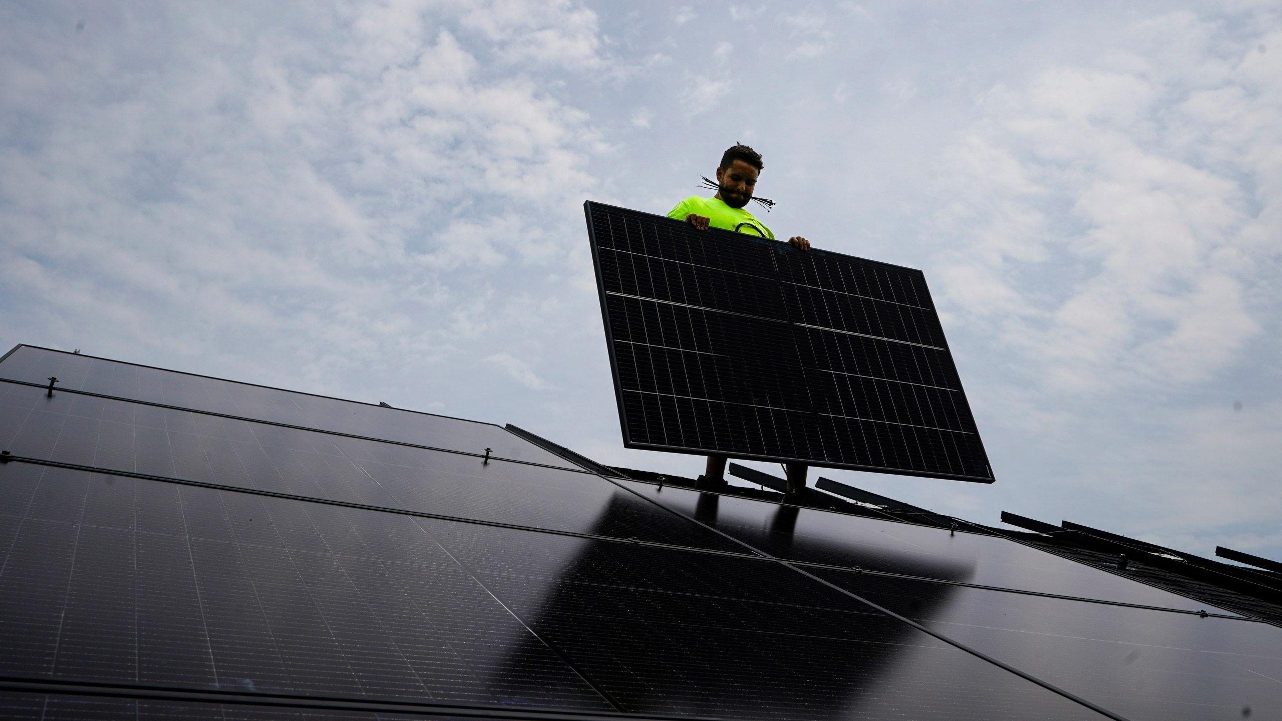 FILE - Nicholas Hartnett, owner of Pure Power Solar, holds a panel as his company installs a solar array on the roof of a home in Frankfort, Ky., July 17, 2023. (AP Photo/Michael Conroy, File)