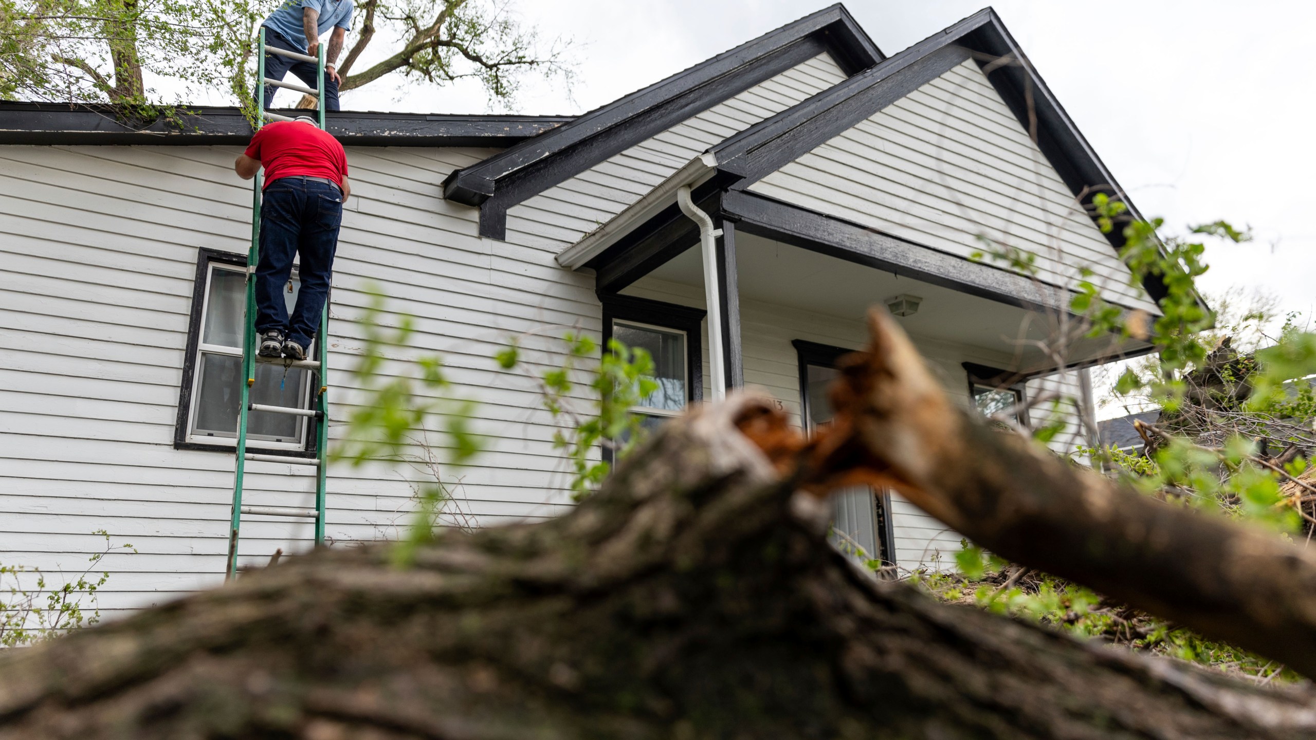 Robert Keesee helps his father, Randy Keesee, up a ladder to access roof damage to their home after a severe storm hit the neighborhood in Council Bluffs, Iowa, on Friday, April 26, 2024. (Anna Reed/Omaha World-Herald via AP)