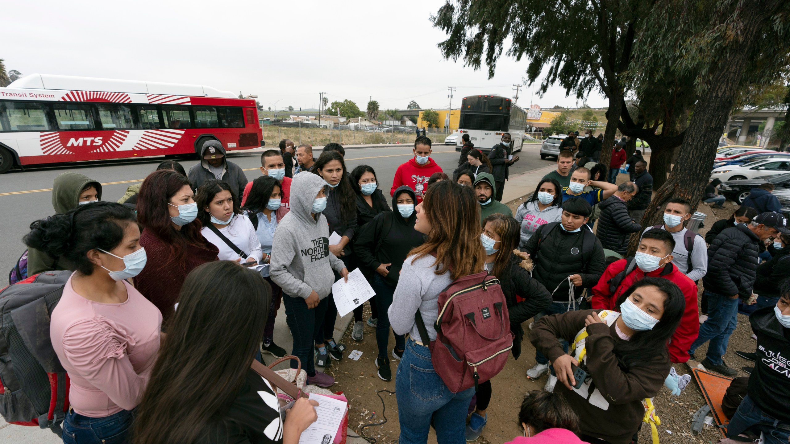 FILE - Migrants listen to a volunteer in a parking lot after being detained and processed for asylum by U.S. authorities, April 12, 2024, in San Diego. A new Biden administration rule aims to speed up asylum processing at the southern border, enabling it to quickly reject a limited group of people believed to have committed serious crimes or who have terrorist links. The change announced May 9 comes during an election year when immigration is a key issue. (AP Photo/Gregory Bull, File)