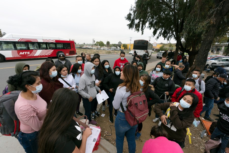 FILE - Migrants listen to a volunteer in a parking lot after being detained and processed for asylum by U.S. authorities, April 12, 2024, in San Diego. A new Biden administration rule aims to speed up asylum processing at the southern border, enabling it to quickly reject a limited group of people believed to have committed serious crimes or who have terrorist links. The change announced May 9 comes during an election year when immigration is a key issue. (AP Photo/Gregory Bull, File)