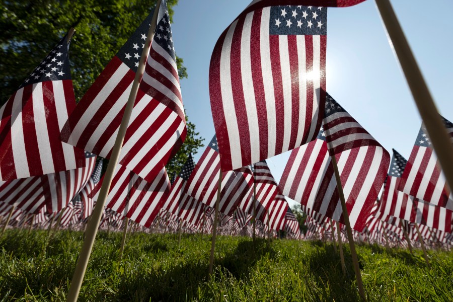 FILE - The sun shines through the flags in the Memorial Day Flag Garden on Boston Common, May 27, 2023, in Boston. Memorial Day is supposed to be about mourning the nation’s fallen service members. But it’s come to anchor the unofficial start of summer and retail discounts. (AP Photo/Michael Dwyer, file)