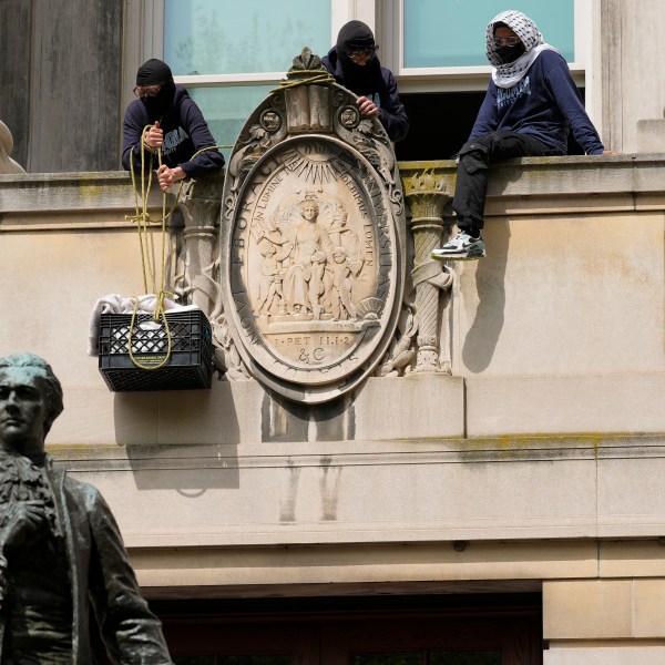 Three people in masks pulling a crate up the side of the building with ropes.