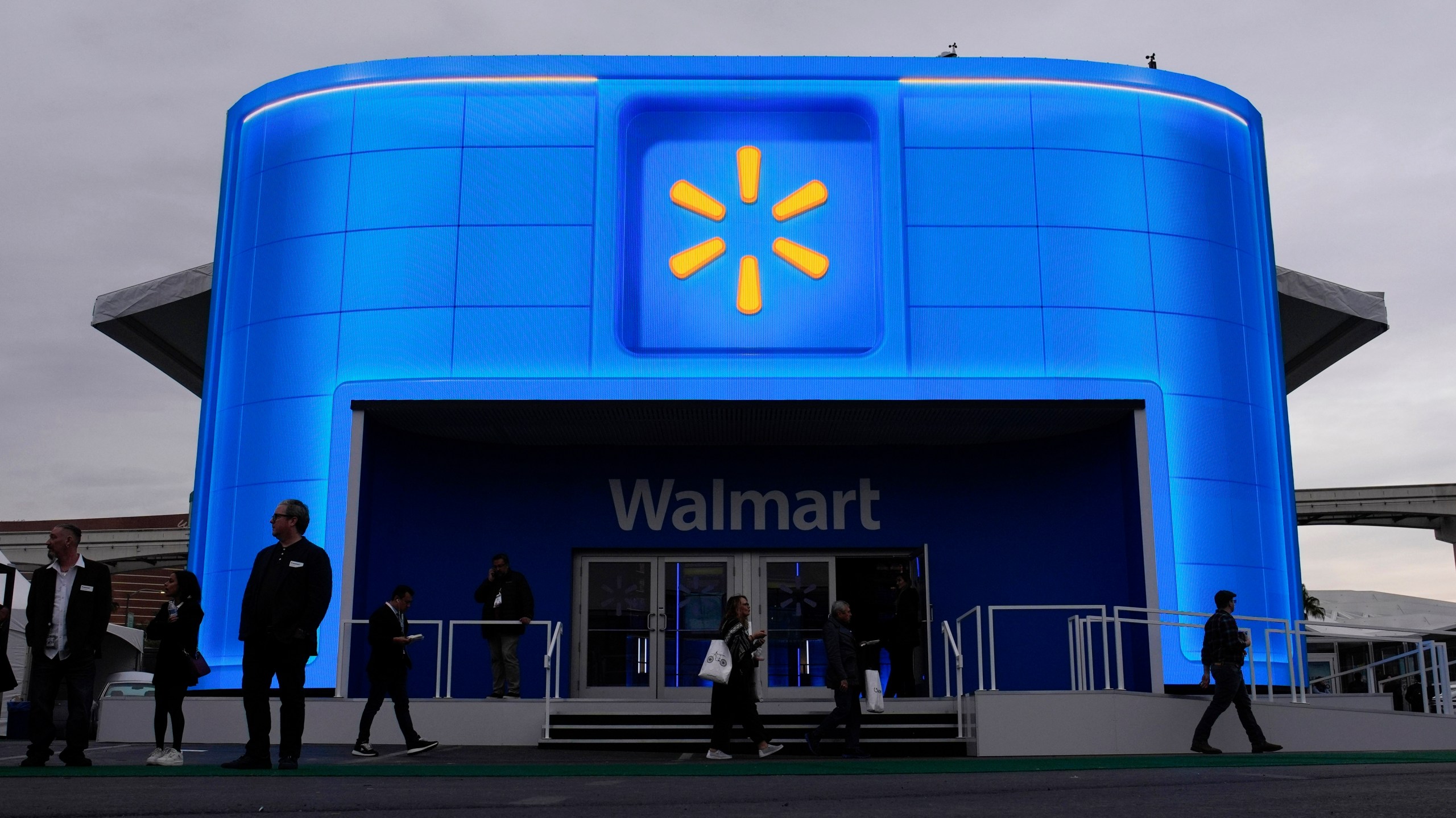 FILE - People walk by the Walmart booth during the CES tech show Tuesday, Jan. 9, 2024, in Las Vegas. Walmart is offering new perks for its hourly workers. They include a new bonus plan as well as opportunities to move into skilled trade jobs within the company. (AP Photo/John Locher, file)