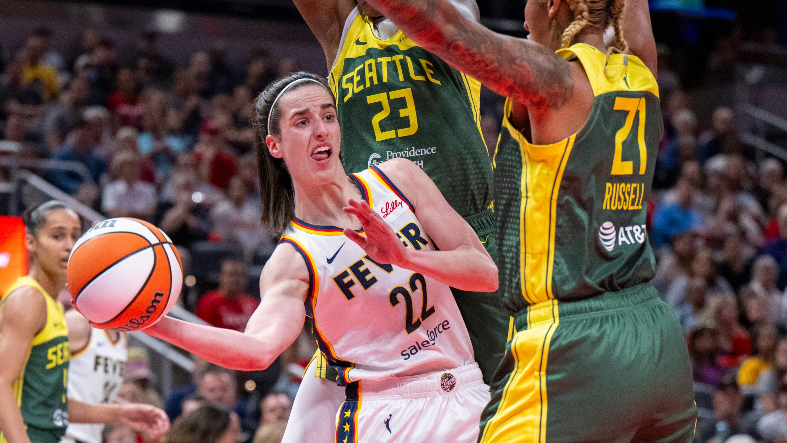 FILE - Indiana Fever guard Caitlin Clark (22) passes the ball from under the basket while being defended by Seattle Storm guard Jordan Horston (23) and center Mercedes Russell (21) during the first half of a WNBA basketball game Thursday, May 30, 2024, in Indianapolis. (AP Photo/Doug McSchooler, File)