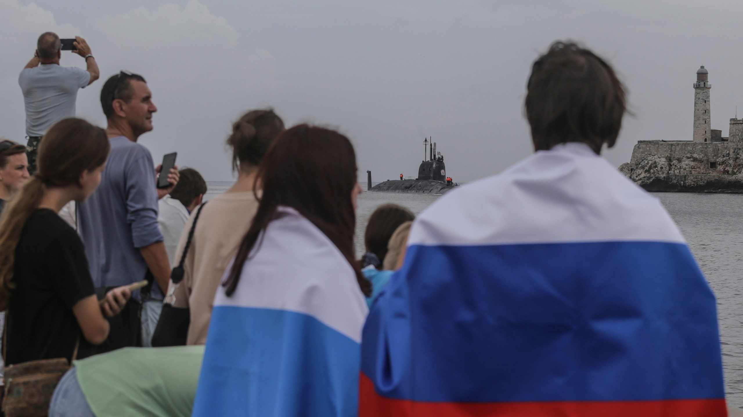 People wearing Russian flags watch the Russian Kazan nuclear-powered submarine arrive at the port of Havana, Cuba, Wednesday, June 12, 2024. A fleet of Russian warships arrived in Cuban waters Wednesday ahead of planned military exercises in the Caribbean. (AP Photo/Ariel Ley)