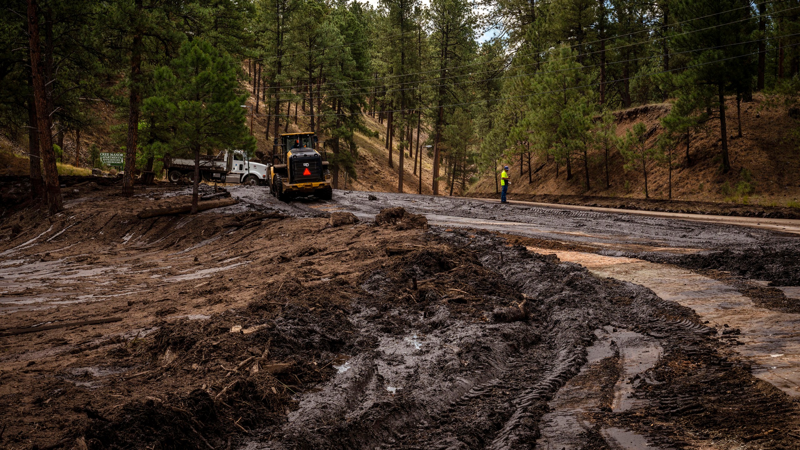 Crews work to remove mud and debris from the aftermath of flooding on Paradise Canyon Drive and Hull Road in Ruidoso, N.M., Monday, June 24, 2024. (Chancey Bush/The Albuquerque Journal via AP)