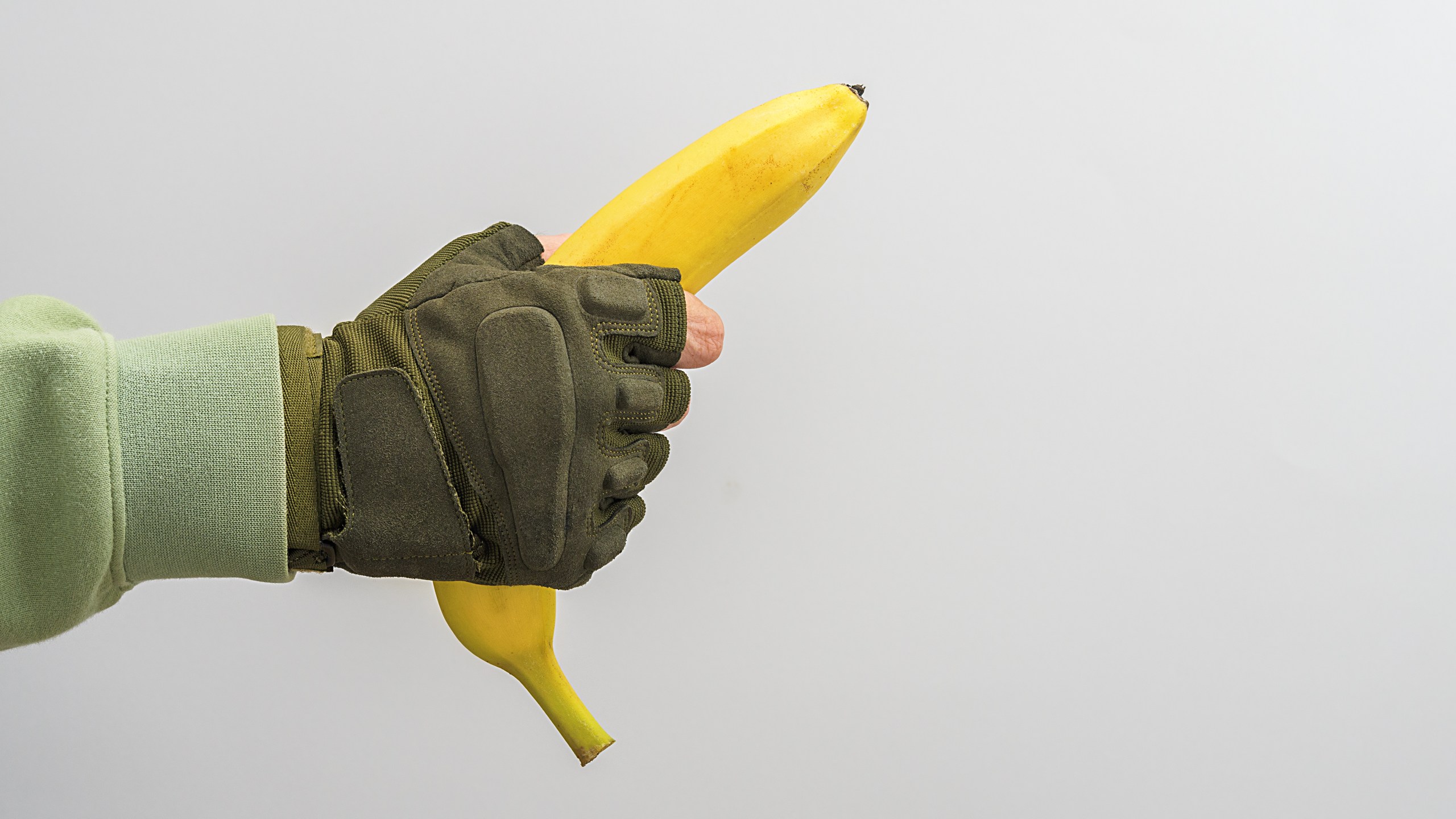 A man's military hand holds a banana on a gray background.