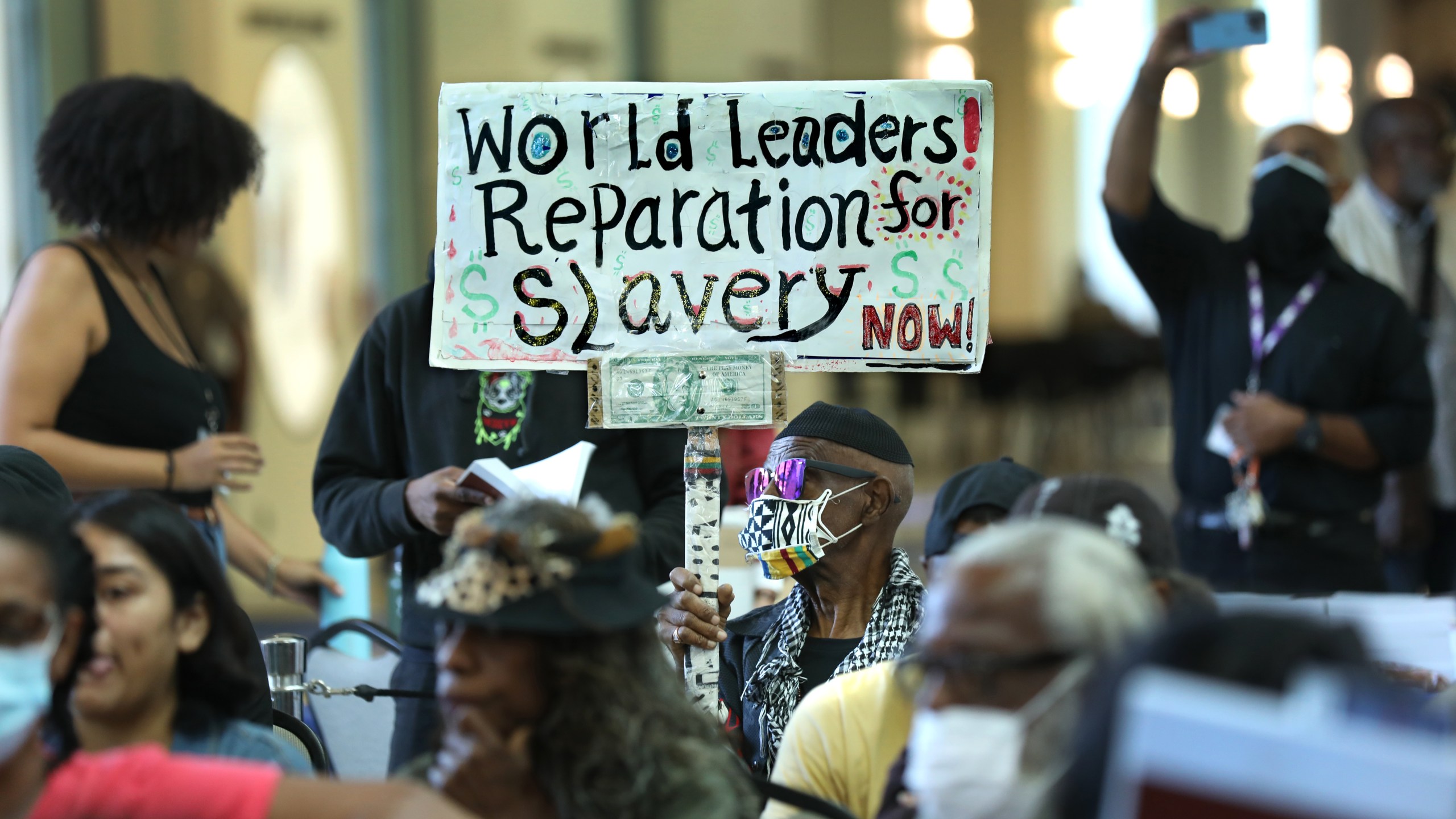 An 80-year-old man holds up a sign urging world leaders to provide reparations in 2022.