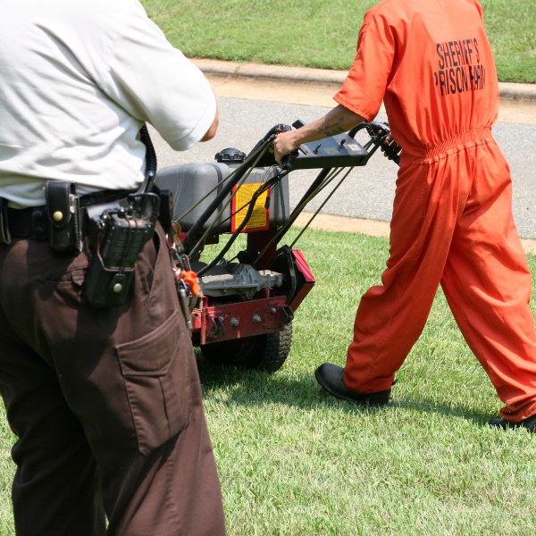 Prisoner working while law enforcement officer keeps watch.