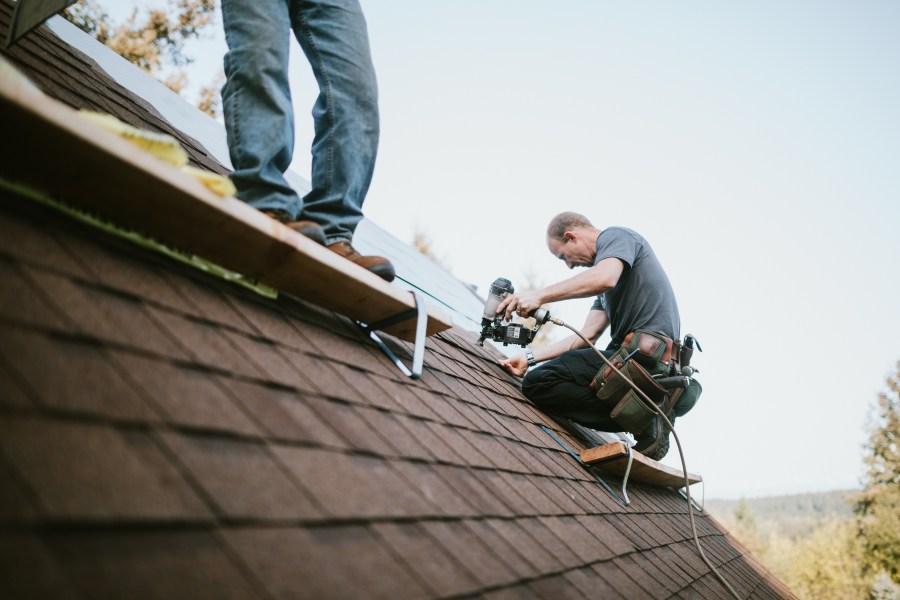 A roofer and crew work on putting in new roofing shingles