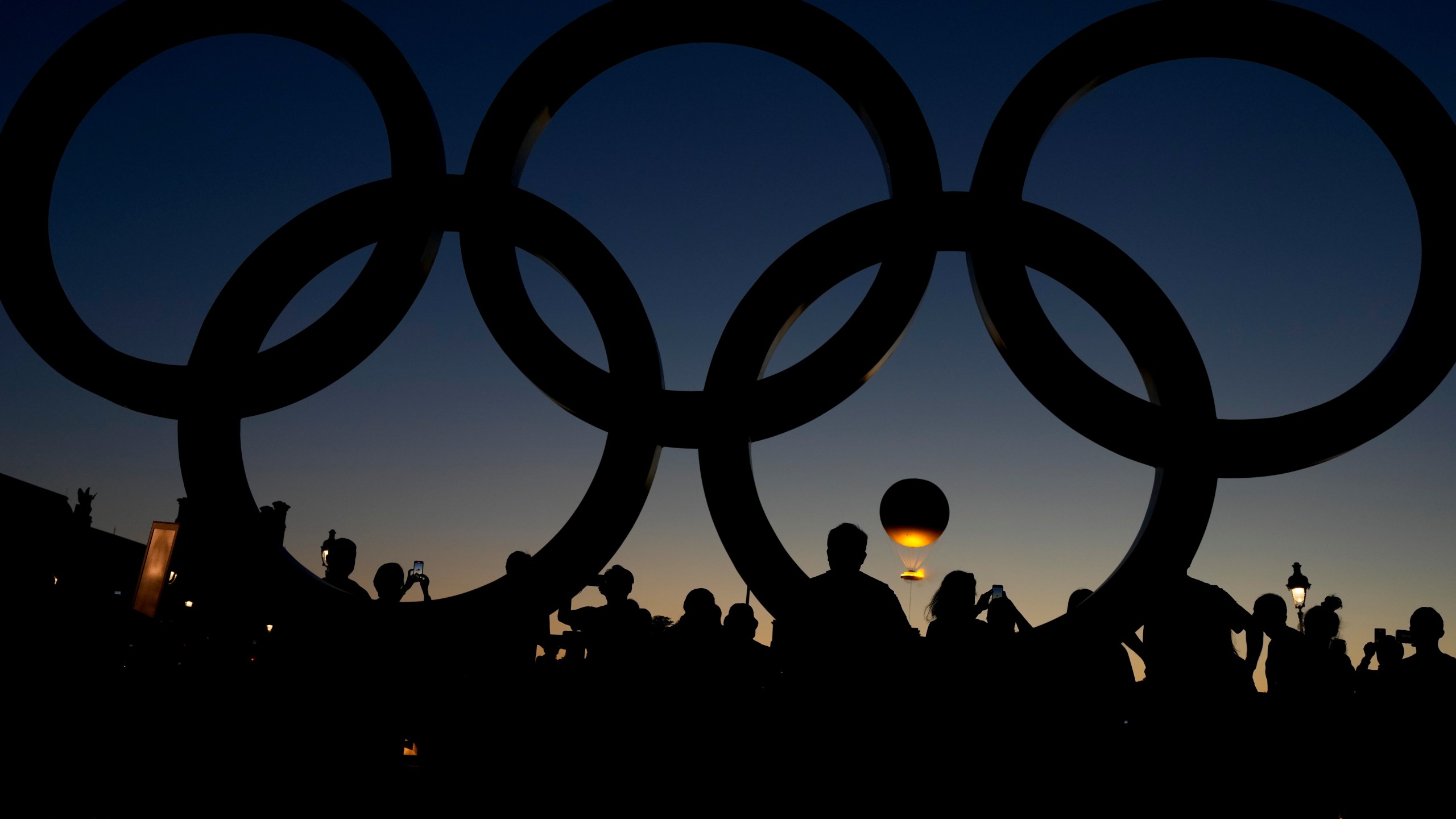 People watch the cauldron rise at sunset by the Olympic rings during the 2024 Summer Olympics, Monday, Aug. 5, 2024, in Paris, France. (AP Photo/Natacha Pisarenko)