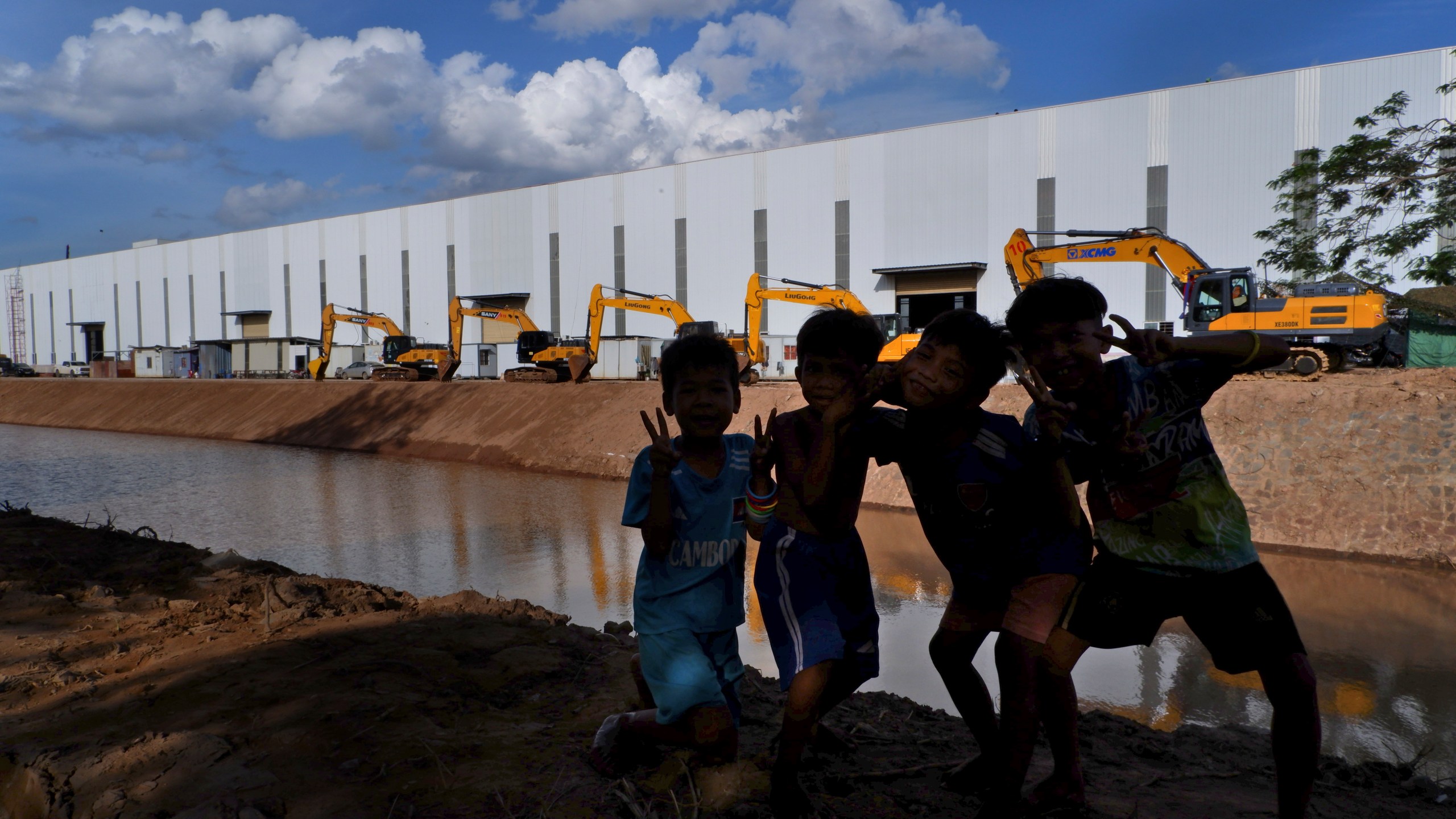 Children pose in front of bulldozers lined along the Funan Techo canal at Prek Takeo village, eastern Phnom Penh, Cambodia, Tuesday, July 30, 2024. (AP Photo/Aniruddha Ghosal)