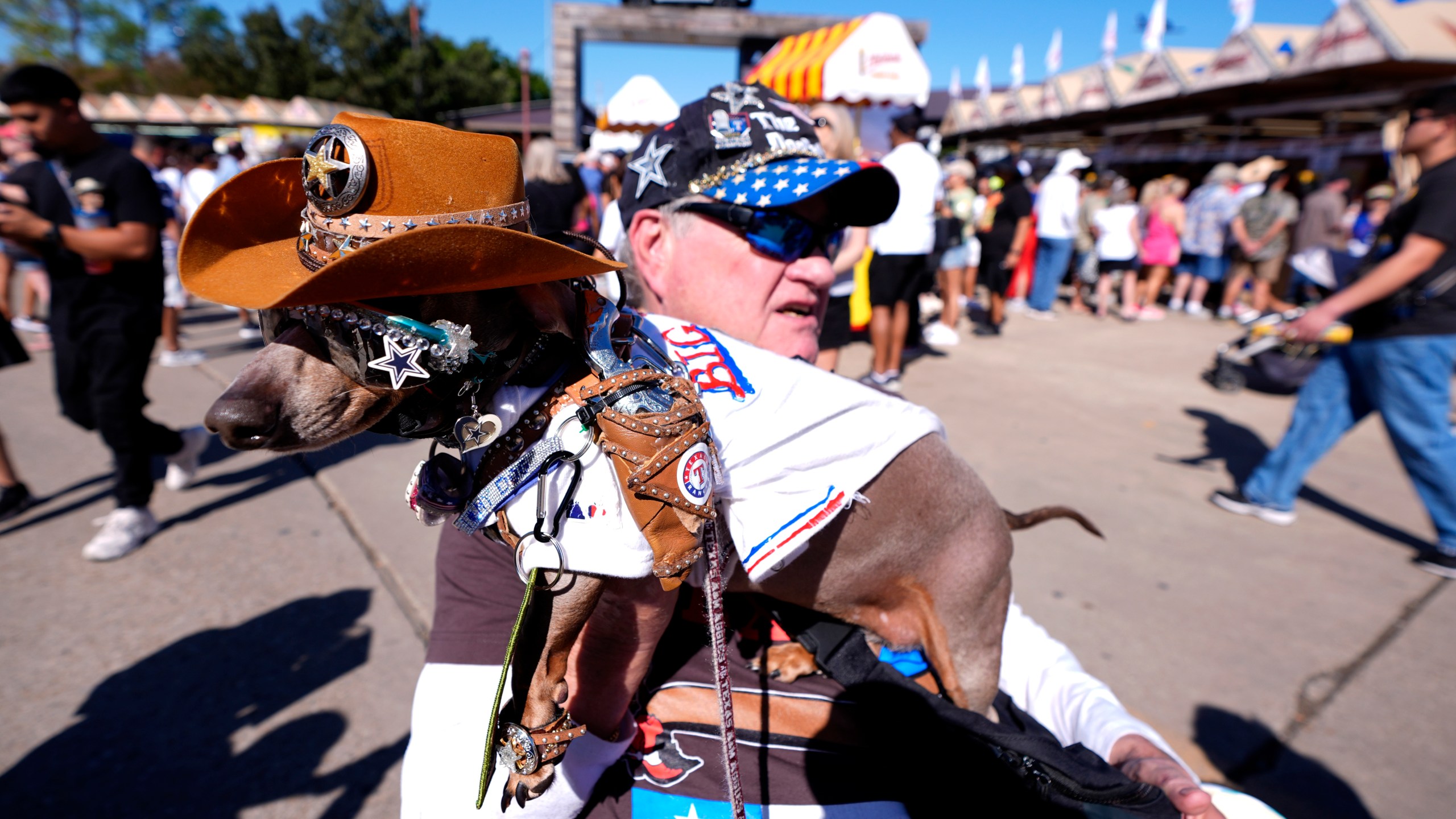 Bob Ankrum holds his service dog, Buttercup, who has a toy pistol fastened on to her shoulder, as they attend the State Fair of Texas in Dallas, on Friday, Sept. 27, 2024. (AP Photo/Tony Gutierrez)