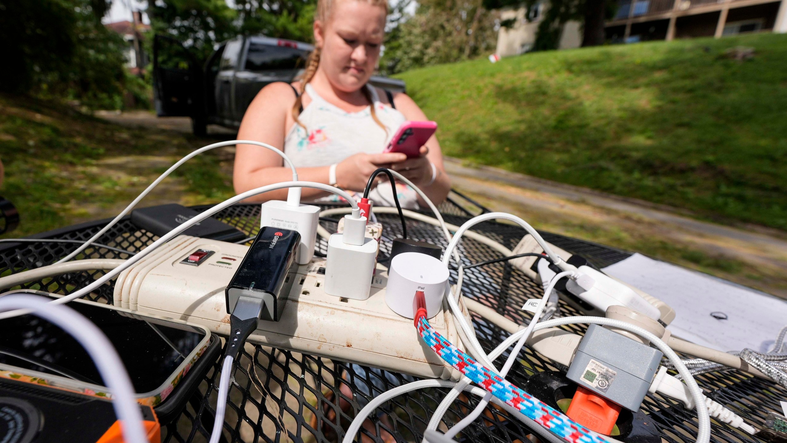 Carrie Owenby looks at her phone as a neighbor with power dropped an extension cord for neighbors who have no power in the aftermath of Hurricane Helene, Monday, Sept. 30, 2024, in Asheville, N.C. (AP Photo/Mike Stewart)