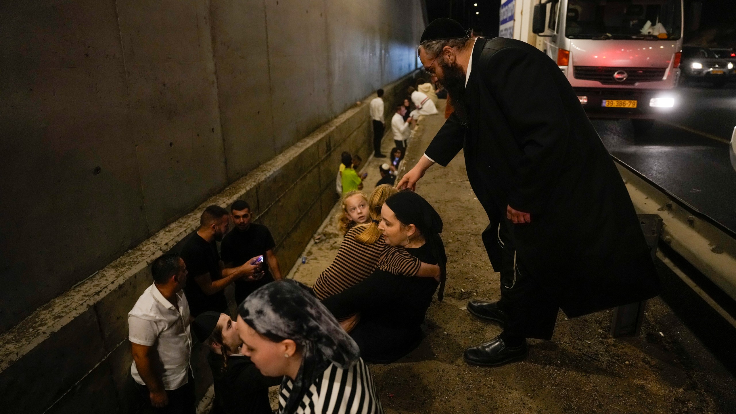 People take cover on the side of a road as a siren sounds a warning of incoming missiles fired from Iran on a freeway in Shoresh, between Jerusalem and Tel Aviv in Israel Tuesday, Oct. 1, 2024. (AP Photo/Ohad Zwigenberg)