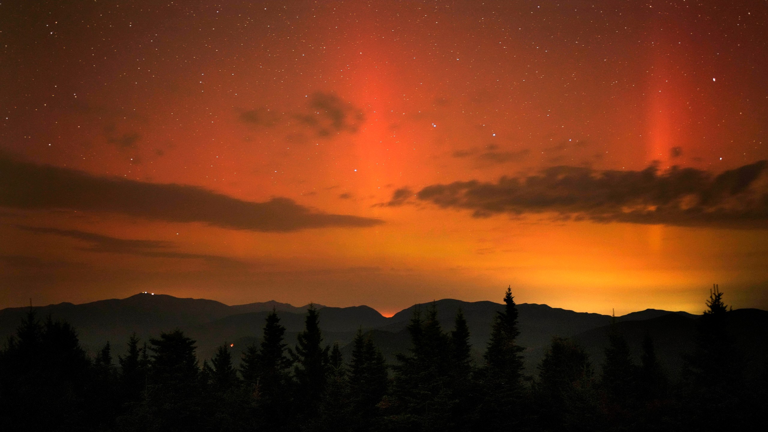 Flares of northern lights color the sky over the White Mountains just after midnight, Friday, Sept. 13, 2024, as viewed from a mountaintop in Chatham, N.H. Lights on the summit of Mount Washington can be seen on the ridgeline at left. (AP Photo/Robert F. Bukaty)