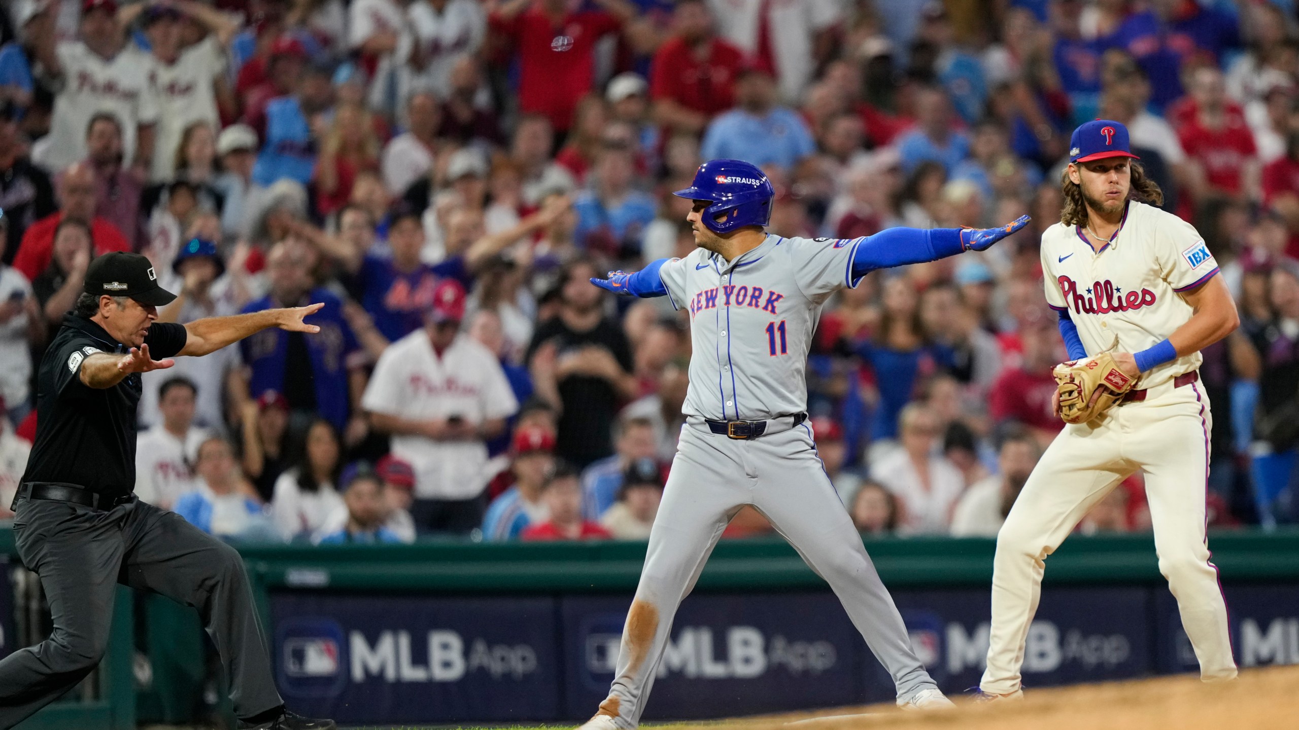 New York Mets' Jose Iglesias reacts past Philadelphia Phillies third base Alec Bohm after making it safely to third on a run scoring single by New York Mets' J.D. Martinez during the eighth inning of Game 1 of a baseball NL Division Series, Saturday, Oct. 5, 2024, in Philadelphia. (AP Photo/Matt Slocum)