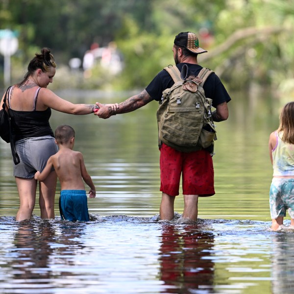 FILE - Dustin Holmes, second from right, holds hands with his girlfriend, Hailey Morgan, while returning to their flooded home with her children Aria Skye Hall, 7, right, and Kyle Ross, 4, in the aftermath of Hurricane Helene, Sept. 27, 2024, in Crystal River, Fla. (AP Photo/Phelan M. Ebenhack, File)