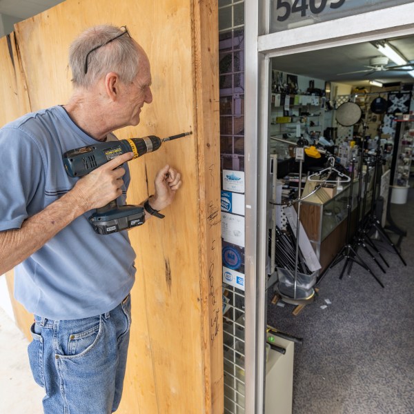 Jim Smetzer puts up boards as his wife Annette clears merchandise from their camera store in preparation for Hurricane Milton on Tuesday, Oct. 8, 2024, in New Port Richey, Fla. (AP Photo/Mike Carlson)