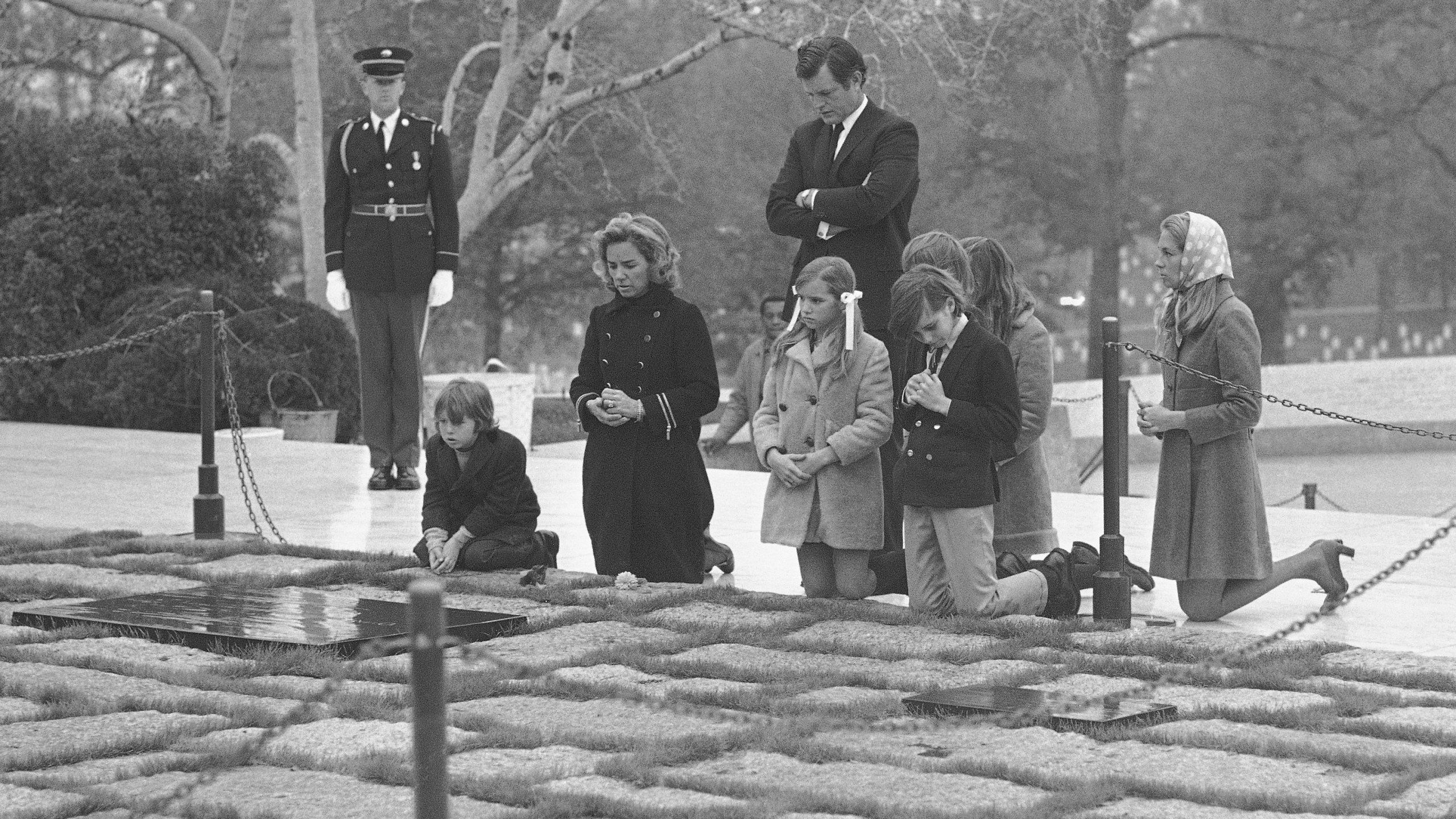 FILE - Sen. Edward Kennedy, back, stands behind the widow of former Senator Robert F. Kennedy, Mrs. Ethel Kennedy, second left, with her five children, and his wife Joan, right, as they pause at the grave of assassinated President John F. Kennedy in Arlington National Cemetery, Nov. 20, 1970, in Arlington, Va. (AP Photo/Bob Daugherty, File)