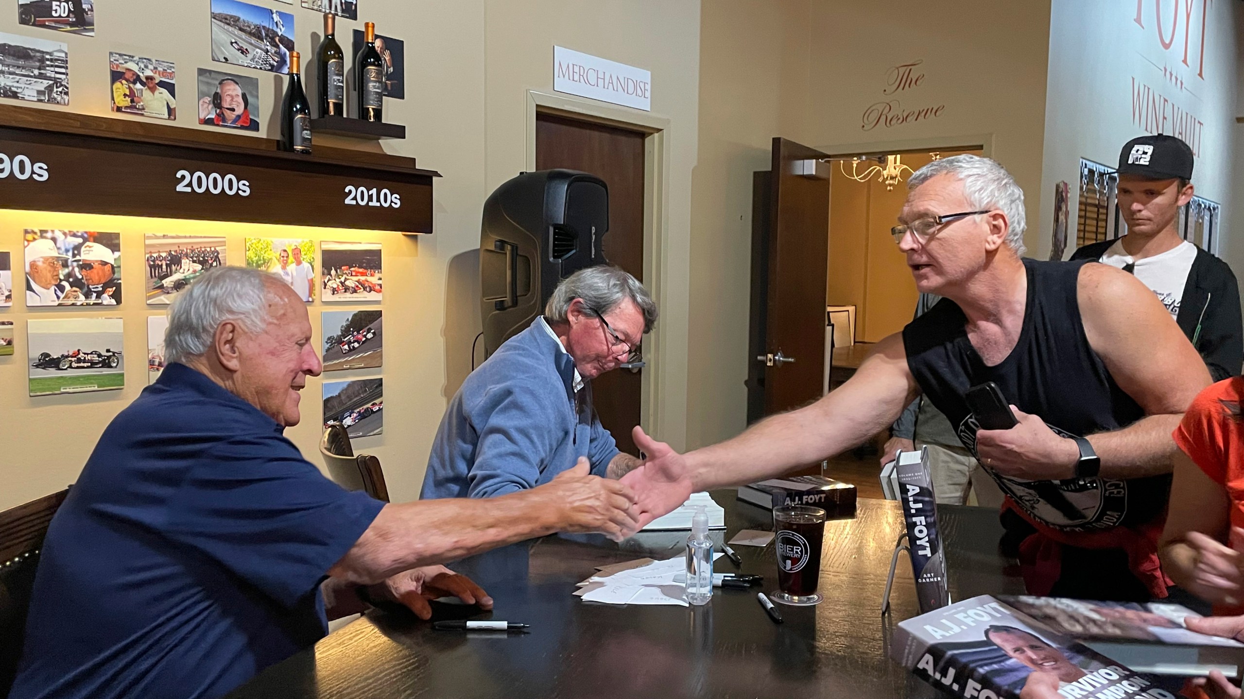 Four time Indianapolis 500 winner A.J. Foyt, left, shakes hands with a fan during a book-signing, Thursday night, Oct. 10, 2024, at the Foyt Wine Vault in Speedway, Ind. Foyt and author Art Garner, center rear, were in town to promote the release of Garner's new biography "A.J. Foyt -- Volume 1: Survivor, Champion, Legend." A second volume has a tentative release date of May 2026. (AP Photo/Michael Marot)