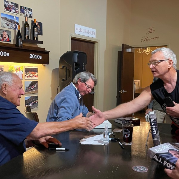 Four time Indianapolis 500 winner A.J. Foyt, left, shakes hands with a fan during a book-signing, Thursday night, Oct. 10, 2024, at the Foyt Wine Vault in Speedway, Ind. Foyt and author Art Garner, center rear, were in town to promote the release of Garner's new biography "A.J. Foyt -- Volume 1: Survivor, Champion, Legend." A second volume has a tentative release date of May 2026. (AP Photo/Michael Marot)