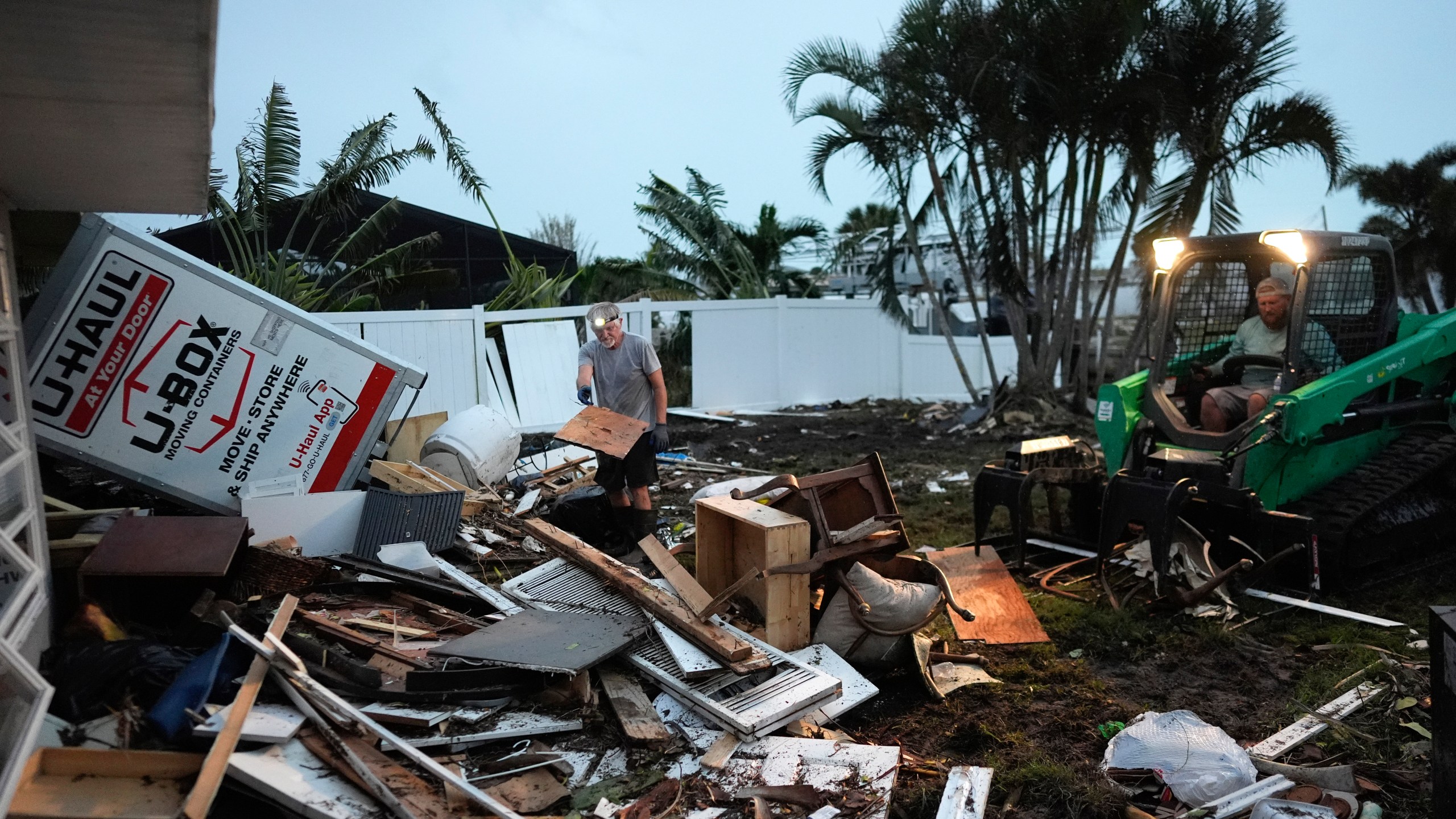 Homeowner Robert Turick, 68, left, and storm waste removal contractor Sven Barnes work to clear debris that Hurricane Milton storm surge swept from other properties into Turick's canal-facing back yard, in Englewood, Fla., Friday, Oct. 11, 2024. Turick, whose family has owned the home for more than 25 years, said it had never flooded until 2022's Hurricane Ian, but since then, it has flooded in three more hurricanes, each bringing higher water levels than the last. (AP Photo/Rebecca Blackwell)