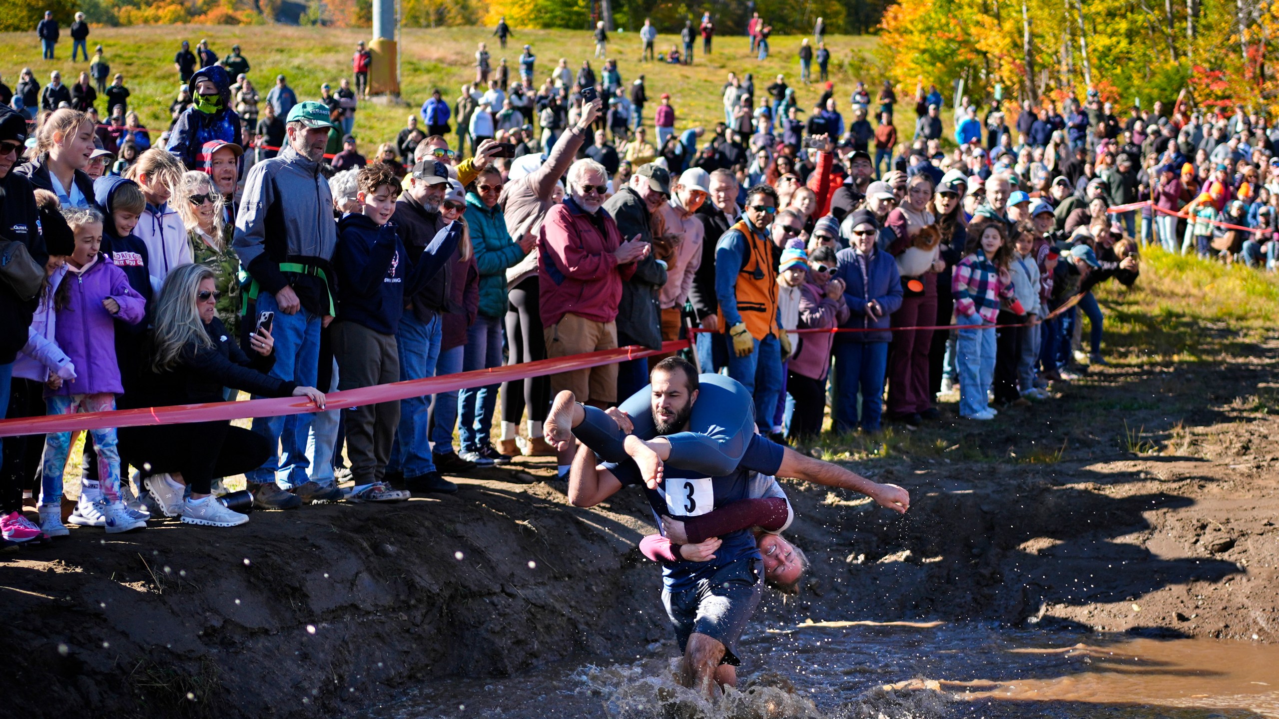 Jon Heaner splashes through the water hazard while carrying Renee Heaner during the North American Wife Carrying Championship, Saturday, Oct. 12, 2024, at Sunday River ski resort in Newry, Maine. (AP Photo/Robert F. Bukaty)