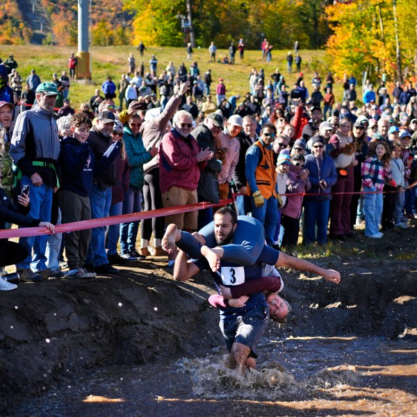 Jon Heaner splashes through the water hazard while carrying Renee Heaner during the North American Wife Carrying Championship, Saturday, Oct. 12, 2024, at Sunday River ski resort in Newry, Maine. (AP Photo/Robert F. Bukaty)