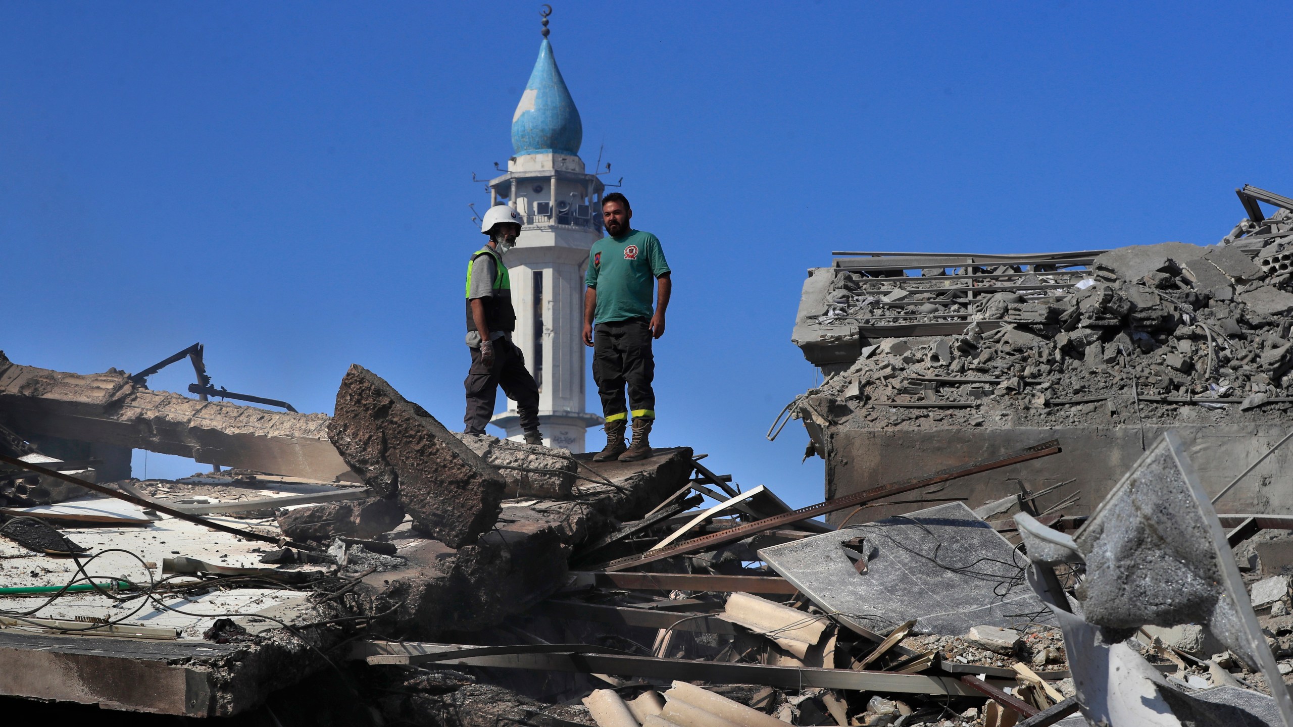 A Hezbollah rescue worker, left, and a Lebanese Civil Defence worker, right, stand on the rubble of destroyed buildings at commercial street that was hit Saturday night by Israeli airstrikes, in NAbatiyeh town, south Lebanon, Sunday, Oct. 13, 2024. (AP Photo/Mohammed Zaatari)