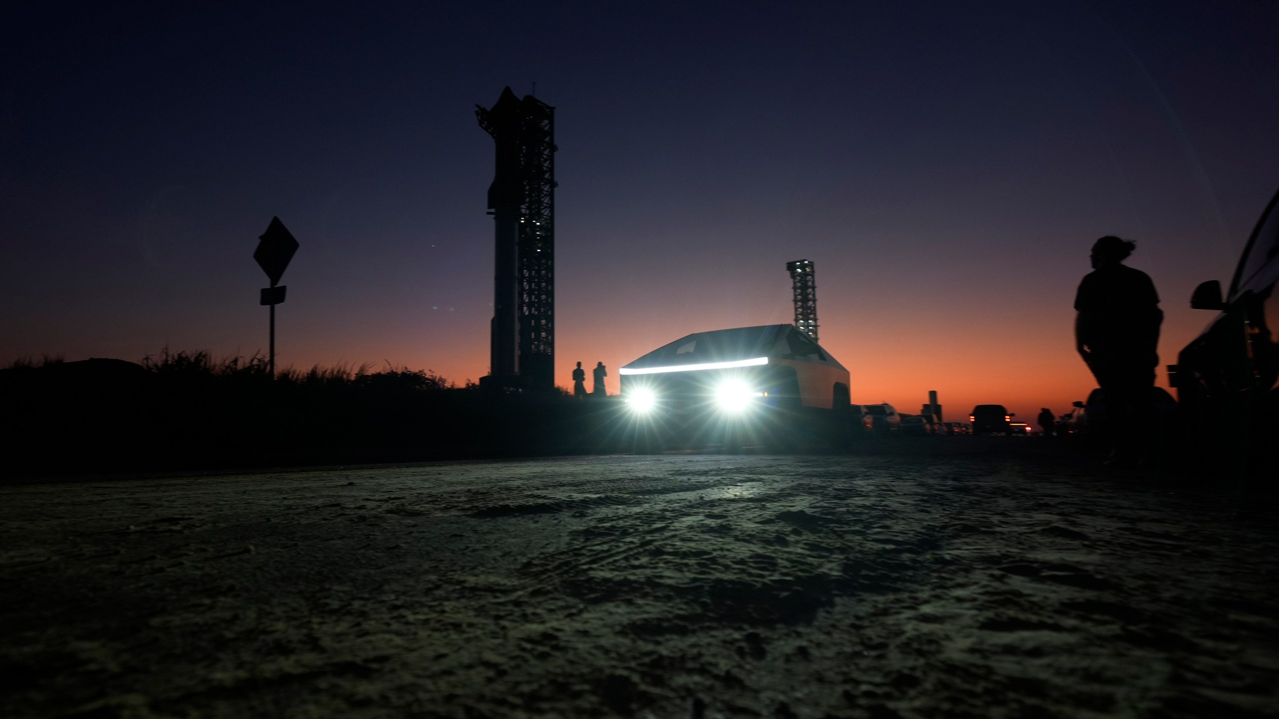 A Tesla Cybertruck passes as the sun sets behind SpaceX's mega rocket Starship, Saturday, Oct. 12, 2024, in Boca Chica, Texas. (AP Photo/Eric Gay)