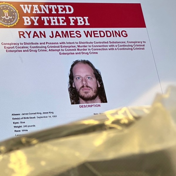 An image of former Canadian Olympic snowboarder Ryan Wedding, 43, who is a fugitive and been charged with allegedly running and participating in a transnational drug trafficking operation, is displayed on a video monitor along with bricks of cocaine, foreground, during a news conference at the FBI offices in Los Angeles, Thursday, Oct. 17, 2024. (AP Photo/Damian Dovarganes)