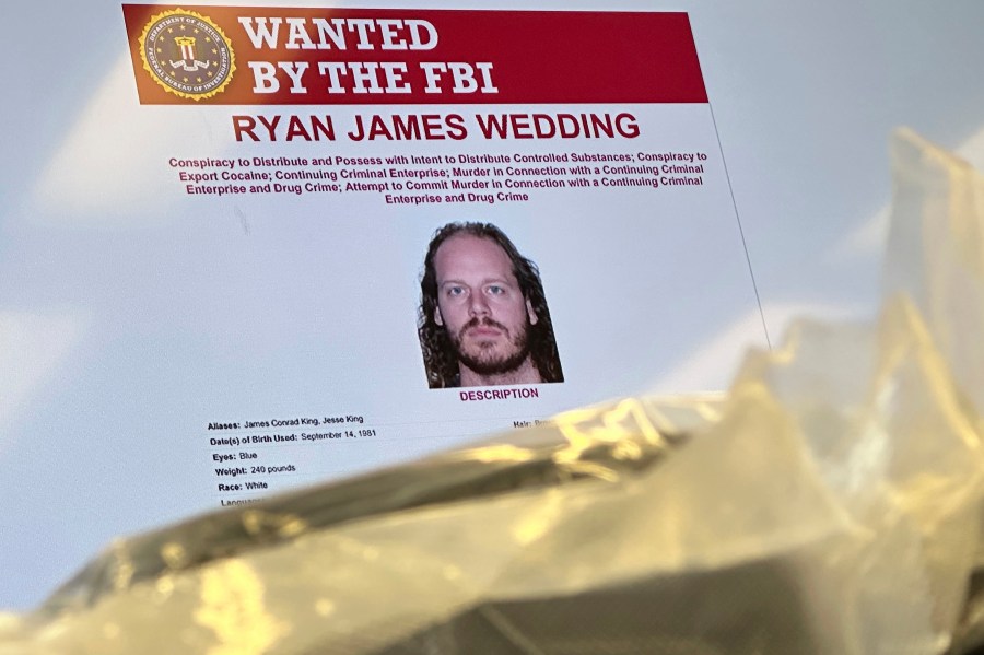 An image of former Canadian Olympic snowboarder Ryan Wedding, 43, who is a fugitive and been charged with allegedly running and participating in a transnational drug trafficking operation, is displayed on a video monitor along with bricks of cocaine, foreground, during a news conference at the FBI offices in Los Angeles, Thursday, Oct. 17, 2024. (AP Photo/Damian Dovarganes)