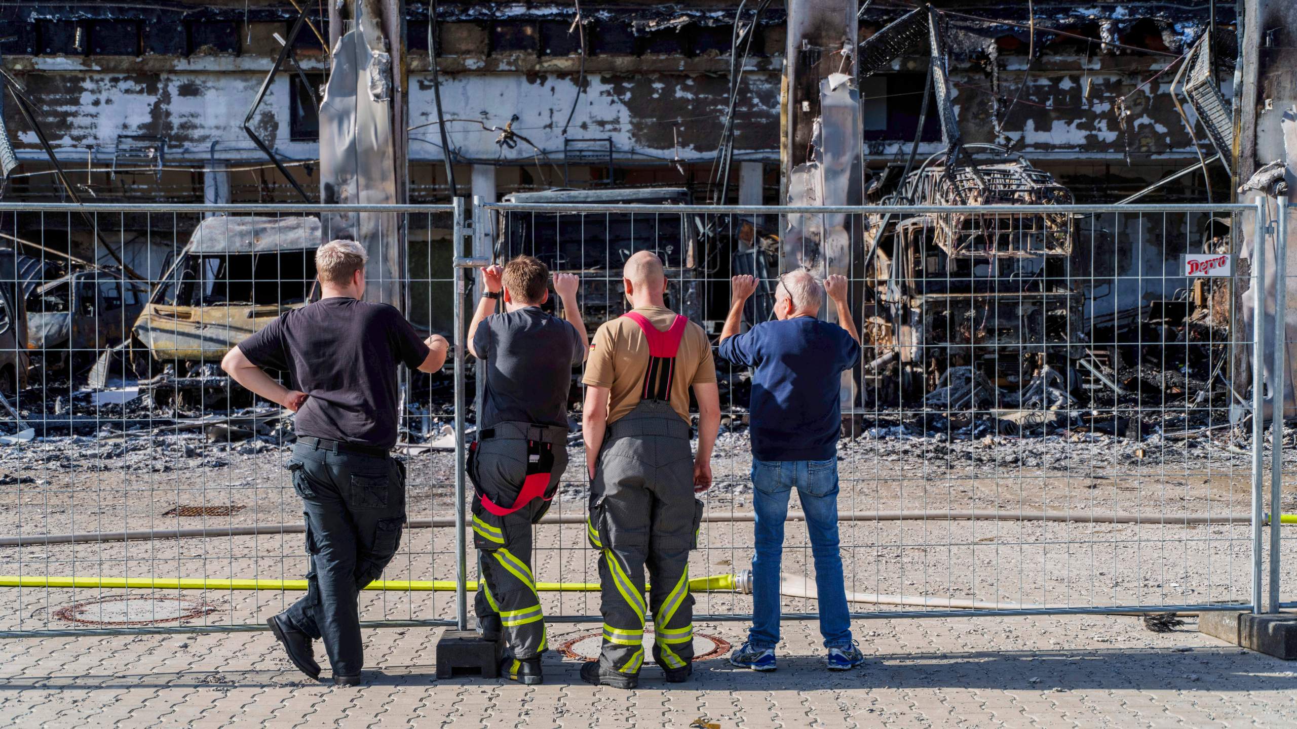 Firefighters stand at the fence and look at the burnt-out equipment, after the new equipment depot of the Stadtallendorf volunteer fire department burnt down with vehicles and equipment, causing millions in damage, in Stadtallendorf, Germany, Wednesday Oct. 16, 2024. (Andreas Arnold/dpa via AP)