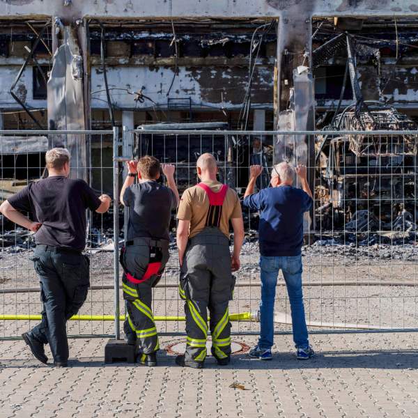 Firefighters stand at the fence and look at the burnt-out equipment, after the new equipment depot of the Stadtallendorf volunteer fire department burnt down with vehicles and equipment, causing millions in damage, in Stadtallendorf, Germany, Wednesday Oct. 16, 2024. (Andreas Arnold/dpa via AP)