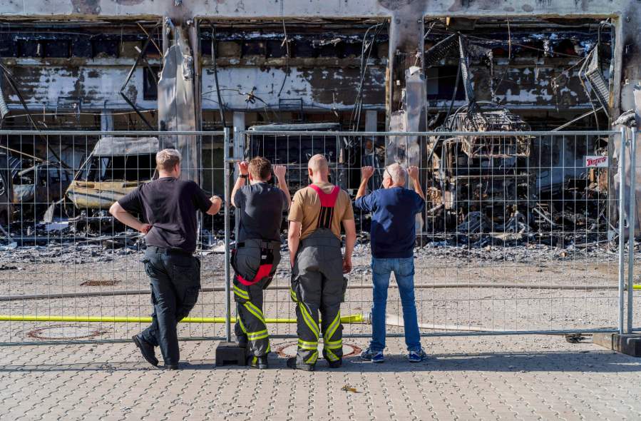 Firefighters stand at the fence and look at the burnt-out equipment, after the new equipment depot of the Stadtallendorf volunteer fire department burnt down with vehicles and equipment, causing millions in damage, in Stadtallendorf, Germany, Wednesday Oct. 16, 2024. (Andreas Arnold/dpa via AP)