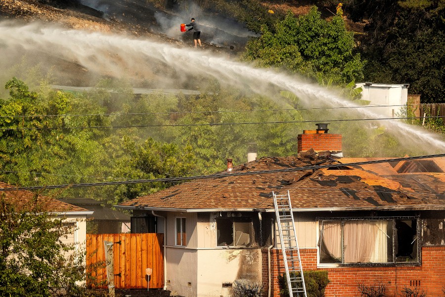 A person dumps water on a grass fire burning above Interstate 580 in Oakland, Calif., Friday, Oct. 18, 2024. (AP Photo/Noah Berger)