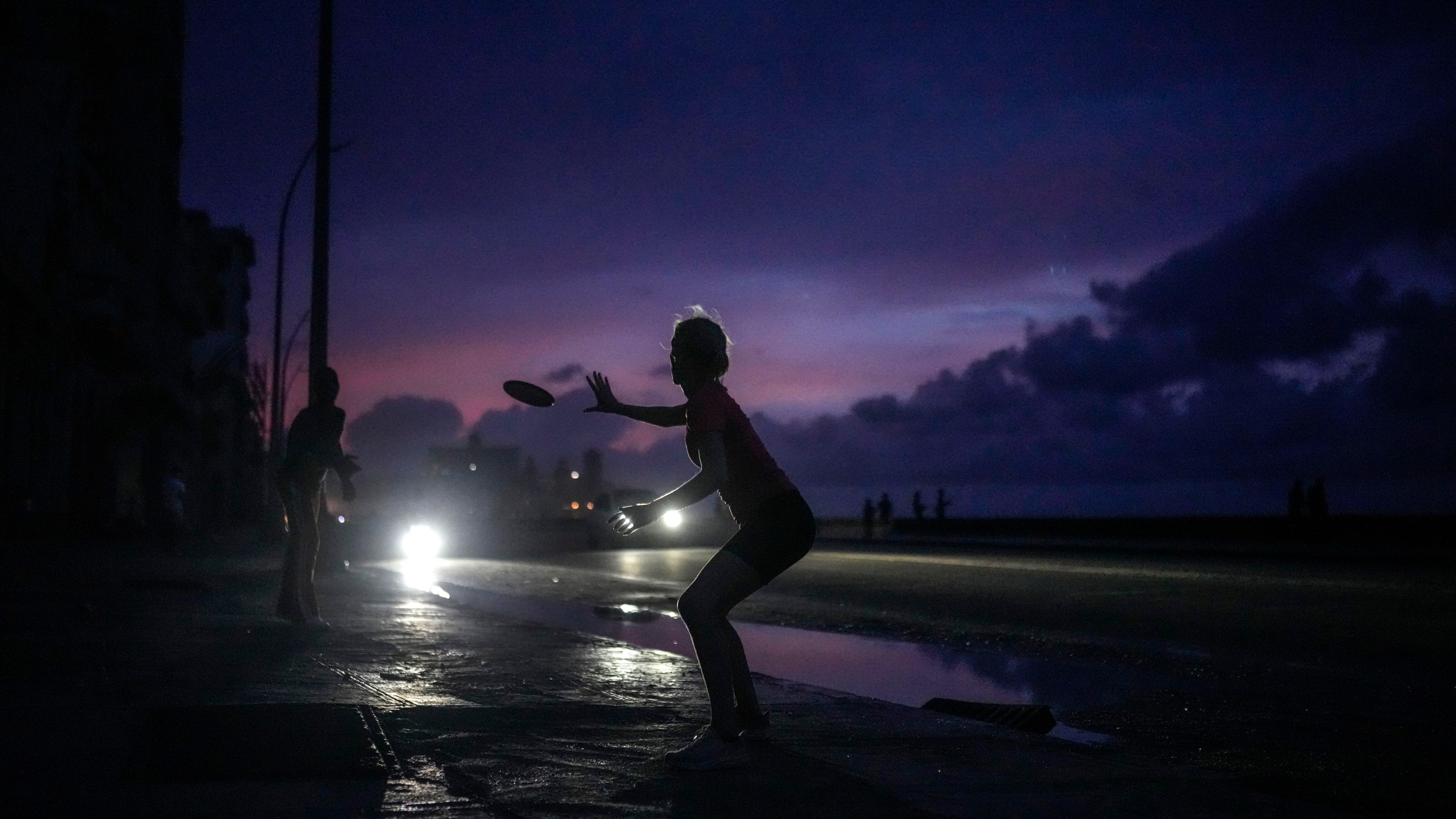 A woman prepares to catch a tossed frisbee during a massive blackout after a major power plant failed in Havana, Cuba, Friday, Oct. 18, 2024. (AP Photo/Ramon Espinosa)