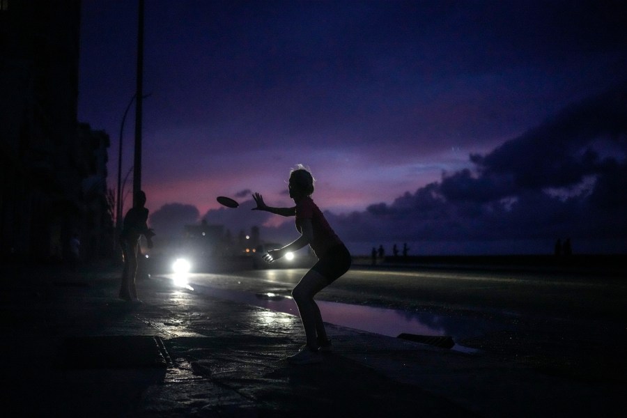 A woman prepares to catch a tossed frisbee during a massive blackout after a major power plant failed in Havana, Cuba, Friday, Oct. 18, 2024. (AP Photo/Ramon Espinosa)