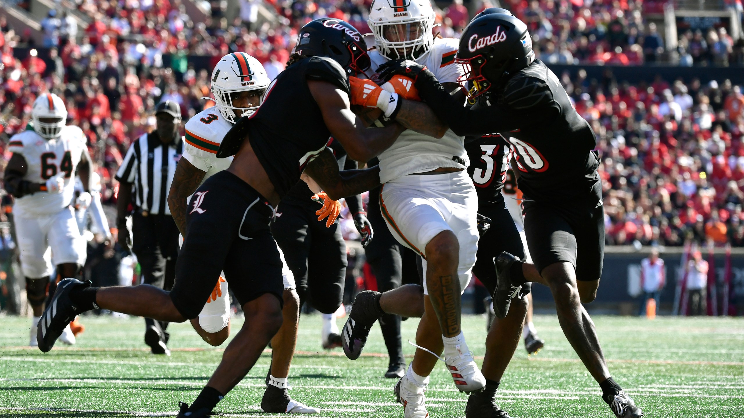 Louisville defensive back Benjamin Perry (10), left, and defensive back Tayon Holloway (20) right, try to bring down Miami running back Damien Martinez (6) during the second half of an NCAA college football game in Louisville, Ky., Saturday, Oct. 19, 2024. Miami won 52-45. (AP Photo/Timothy D. Easley)