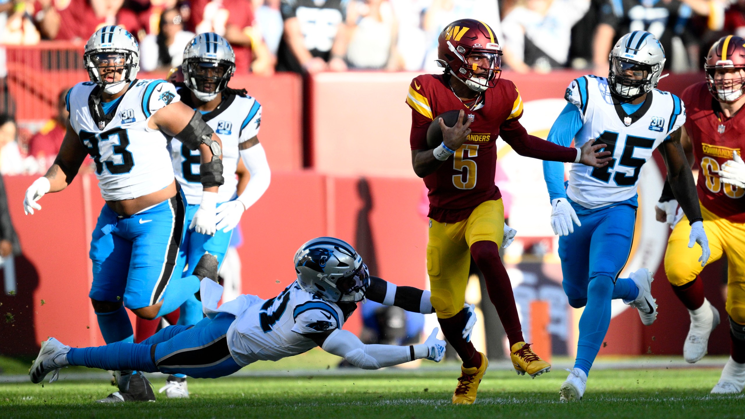 Washington Commanders quarterback Jayden Daniels (5) runs from Carolina Panthers safety Nick Scott (21) and linebacker Marquis Haynes Sr. (45) during the first half of an NFL football game, Sunday, Oct. 20, 2024, in Landover, Md. (AP Photo/Nick Wass)