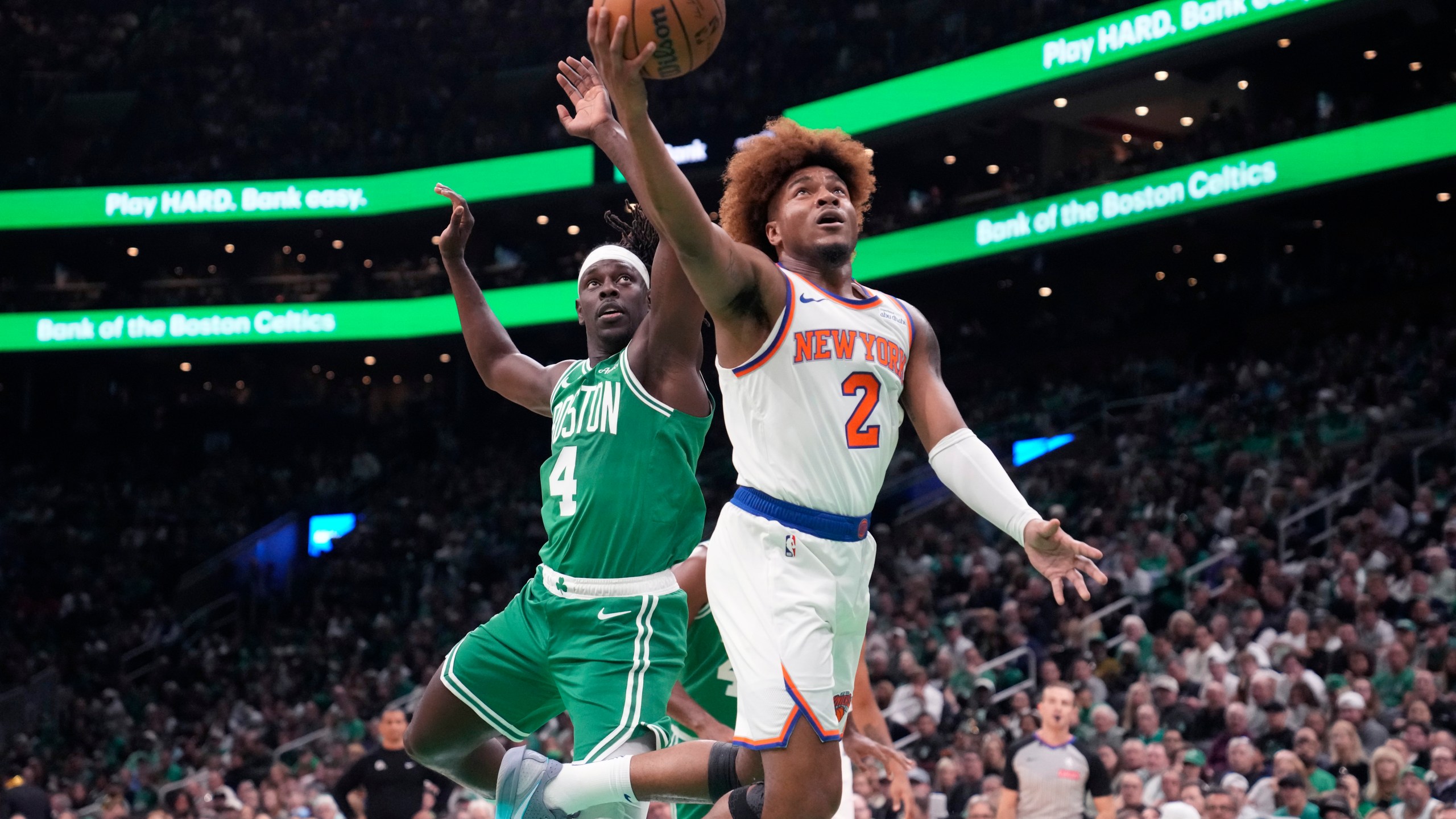 New York Knicks guard Miles McBride (2) drives to the basket past Boston Celtics guard Jrue Holiday (4) during the first half of an NBA basketball game, Tuesday, Oct. 22, 2024, in Boston. (AP Photo/Charles Krupa)