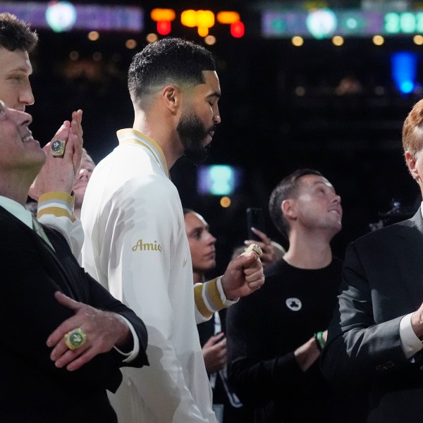 Boston Celtics forward Jayson Tatum, center, admires his ring as the 2024 World Championship banner is raised prior to an NBA basketball game against the New York Knicks, Tuesday, Oct. 22, 2024, in Boston. With Tatum are team owners Wyc Grousbeck, left, and Steve Pagliuca. (AP Photo/Charles Krupa)