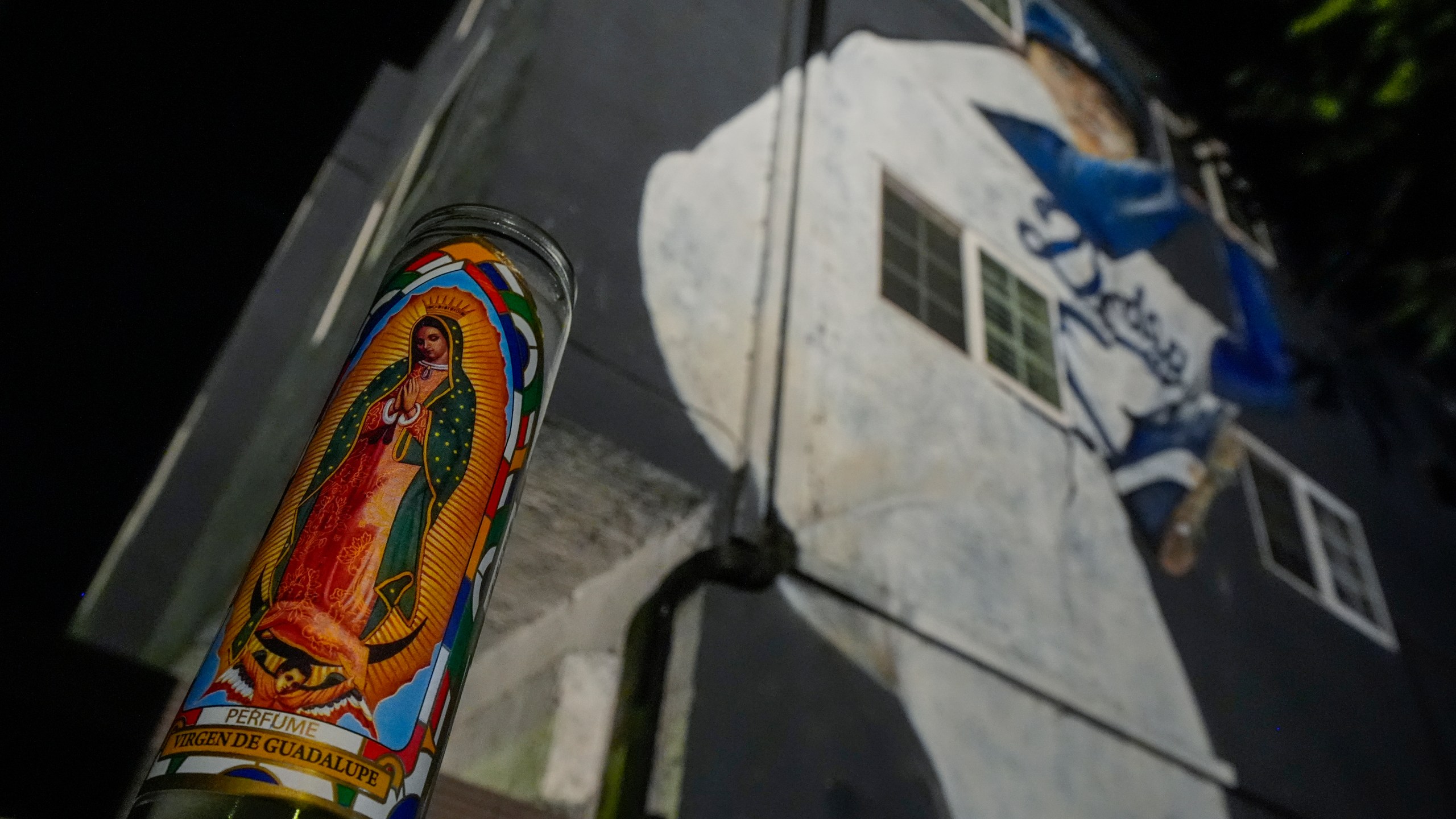 A votive candle donning an image of the Virgen de Guadalupe sits near a mural depicting former Los Angeles Dodgers pitcher Fernando Valenzuela, Tuesday, Oct. 22, 2024, in Los Angeles. (AP Photo/Julio Cortez)