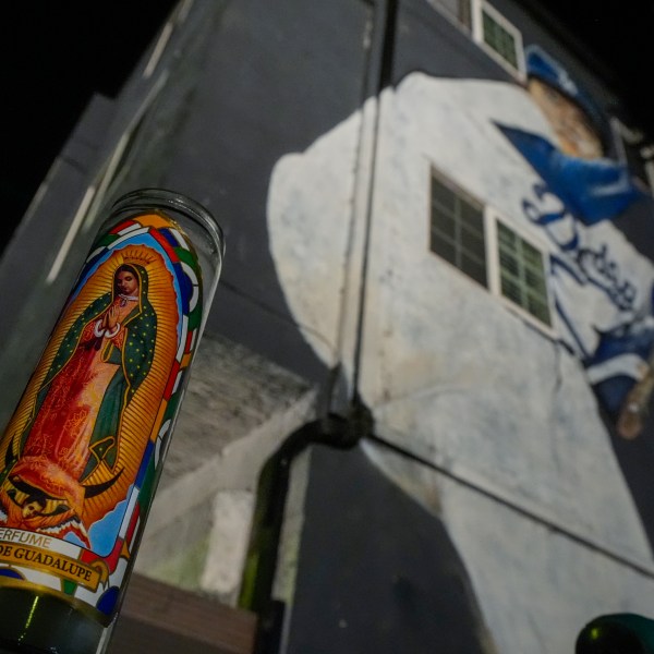 A votive candle donning an image of the Virgen de Guadalupe sits near a mural depicting former Los Angeles Dodgers pitcher Fernando Valenzuela, Tuesday, Oct. 22, 2024, in Los Angeles. (AP Photo/Julio Cortez)