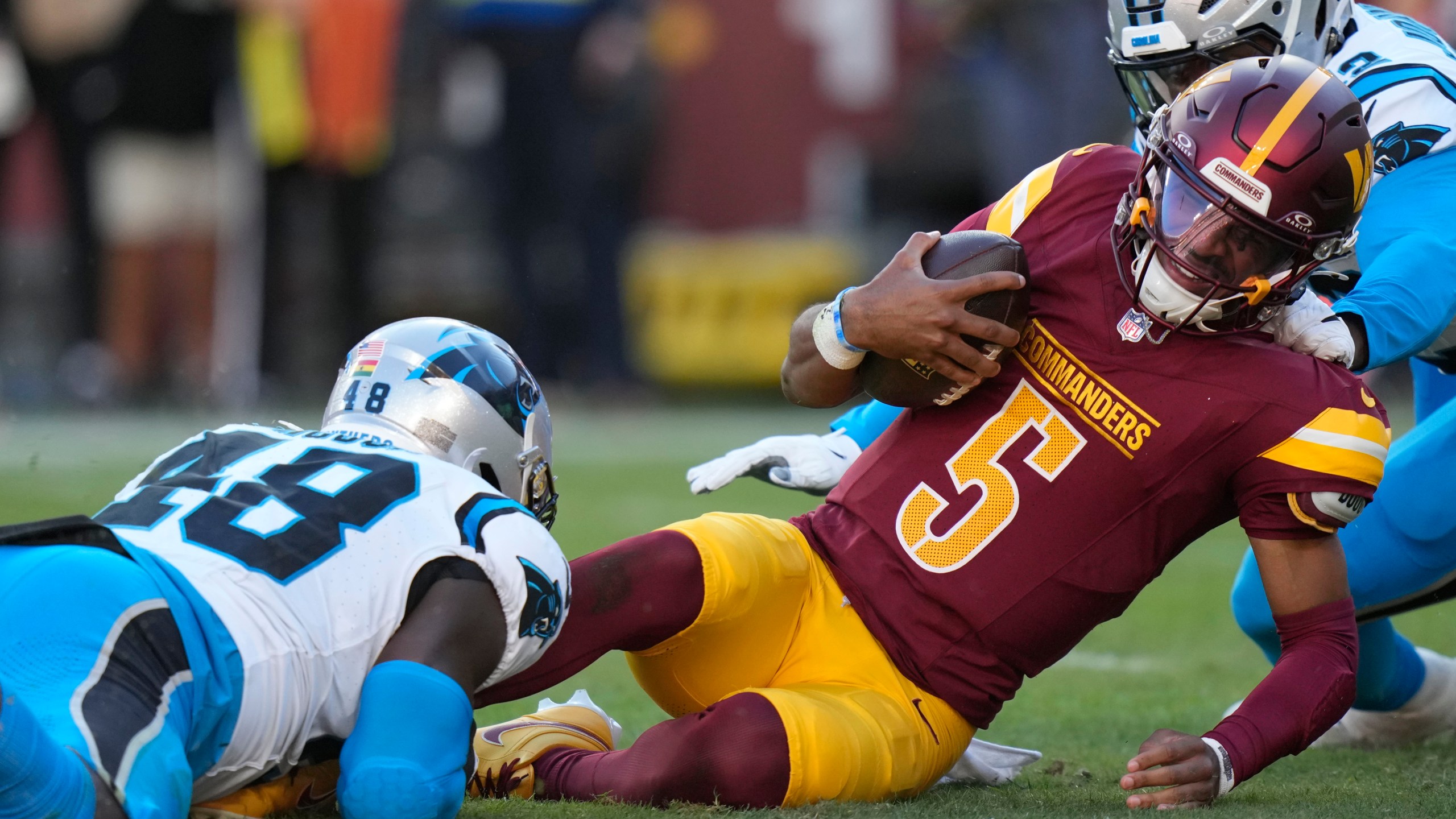 Washington Commanders quarterback Jayden Daniels (5) is tackled by Carolina Panthers linebacker Thomas Incoom (48) during the first half of an NFL football game, Sunday, Oct. 20, 2024, in Landover, Md. (AP Photo/Stephanie Scarbrough)